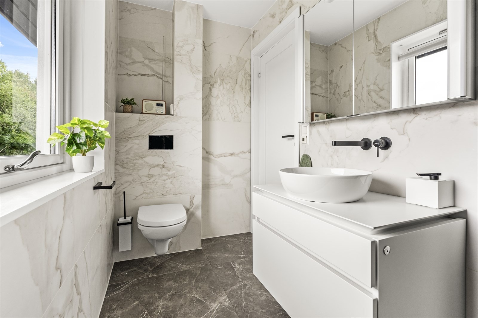 Badet er innredet med vegghengt wc, servantinnredning, overskap med speildører og dusj med svingbar glassdør Galleribilde