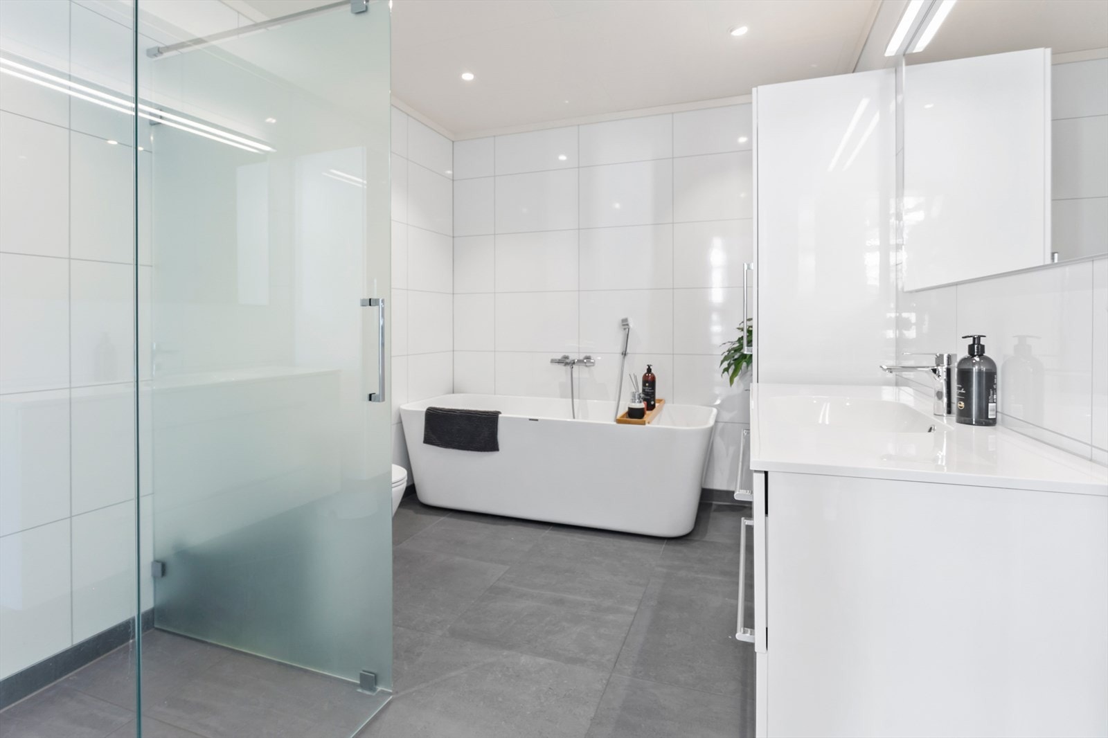 Badet er utstyrt med badekar, dusjhjørne med glassdør, helstøpt kompositt servantplate med vask, høyskap, speil og wc Galleribilde