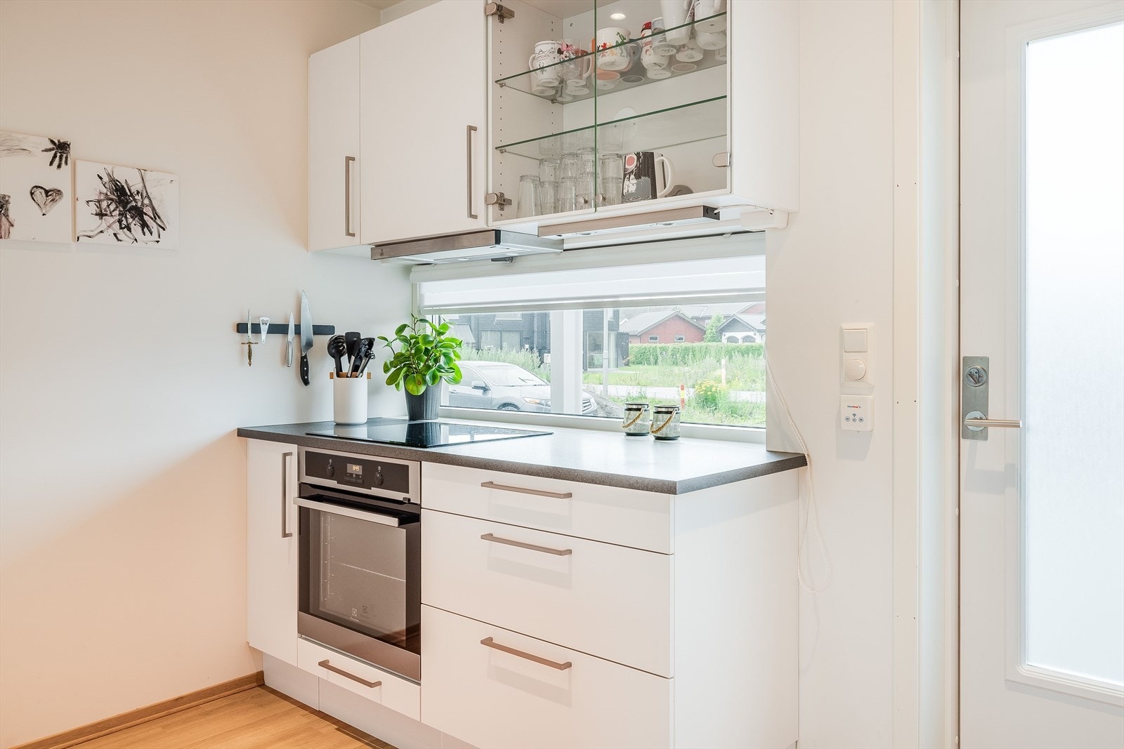 Innredningen har hvite glatte fronter og laminert benkeplate. Det ene overskapet har glassdører og glasshyller inni. Galleribilde