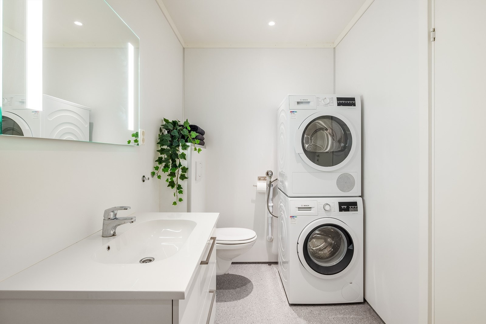 Lyst og moderne bad/vaskerom fra 2025 med våtromsbelegg på gulv med gulvvarme, lyse våtromsplater på veggene og downlights i himlingen. Plass og opplegg for vaskemaskin og tørketrommel over om ønskelig. Galleribilde