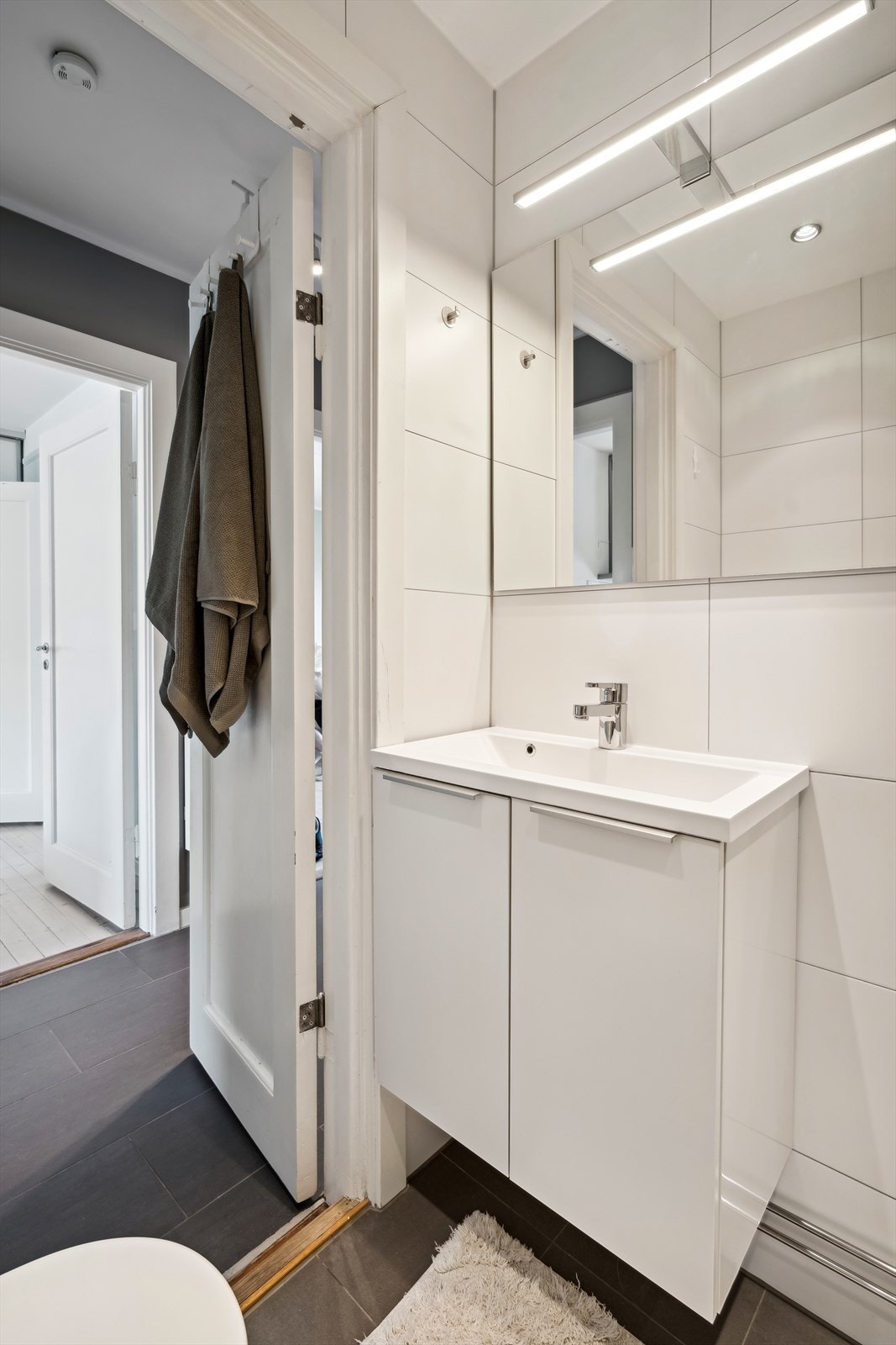 Badet er innredet med veggmonterte dusjvegger, dusj direkte på gulv med termostat batteri, klosett, servant med skapinnredning, speil med belysning og opplegg for vaskemaskin. Galleribilde