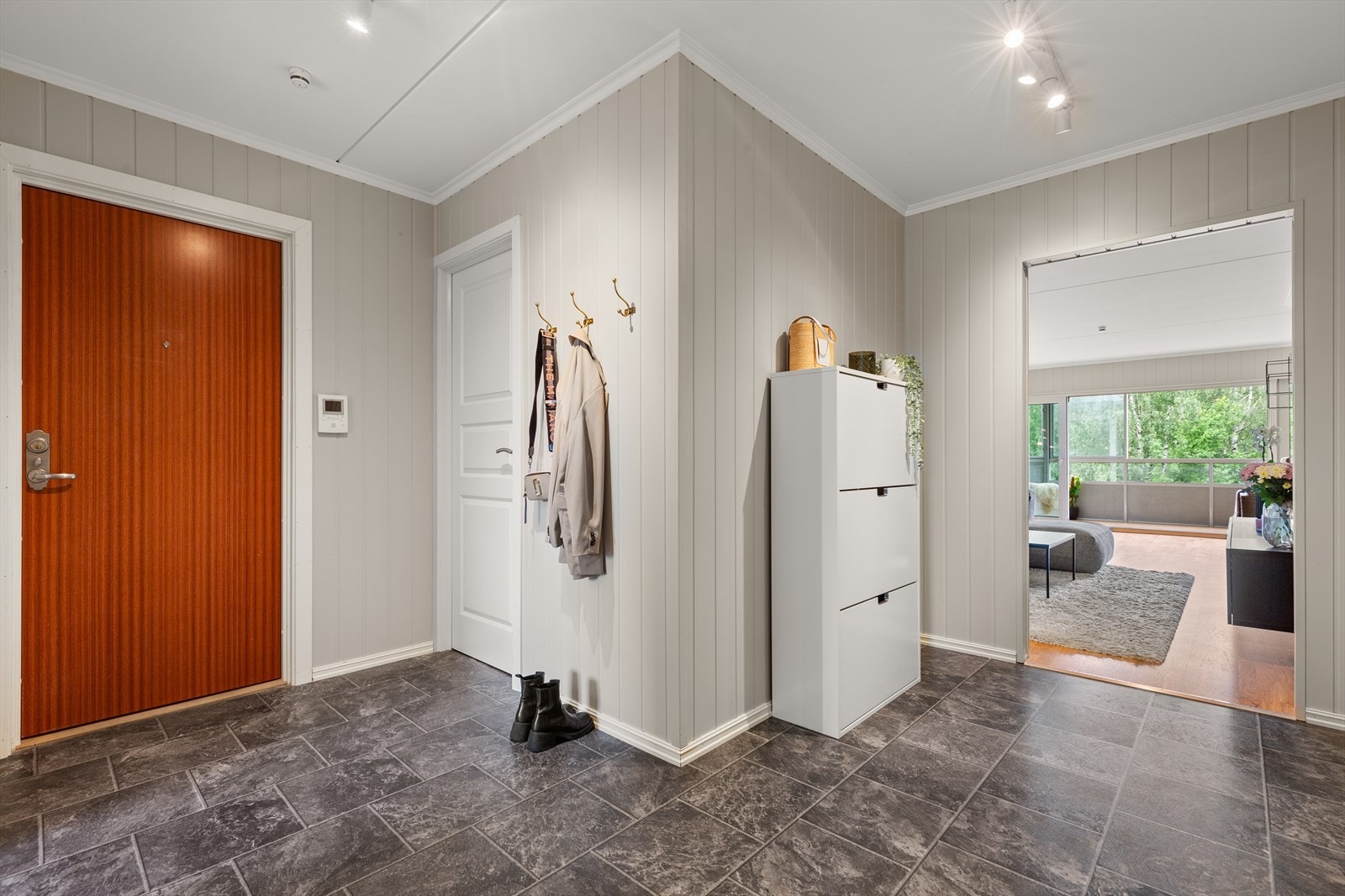 Entreen har belegg på gulv, panel på vegger, og hvite innerdører. Entreen har oppheng på vegg og inngang til en bod/garderobe som gjør det enkelt å holde orden. Galleribilde