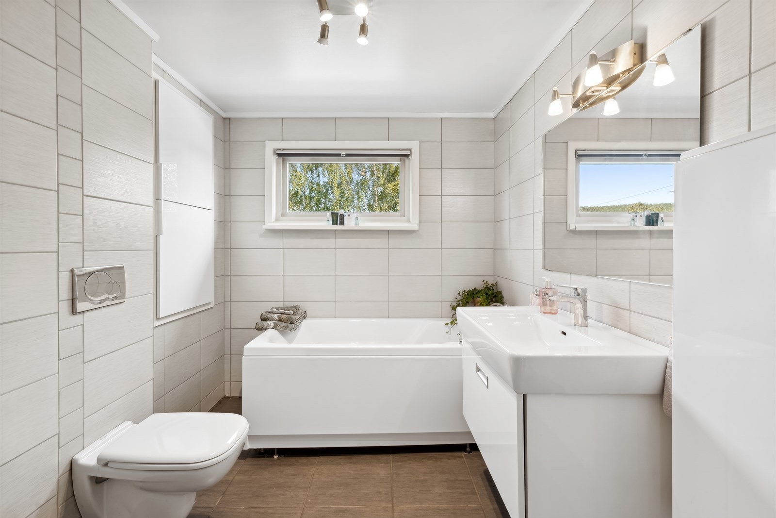 Vegghengt toalett og innebygget sisterne. Servantinnredning med hvit glatt front, heldekkende porselenservant, ettgreps servantarmatur og speil med belysning. Galleribilde