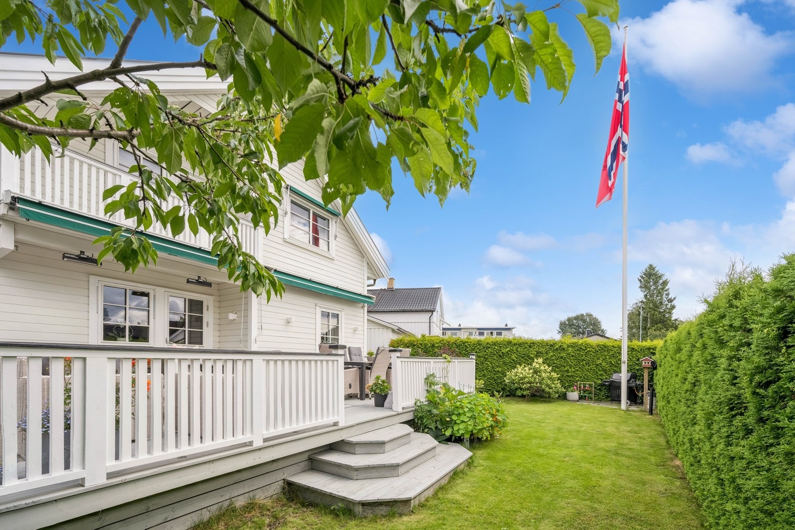 Fra terrassen er det utgang til hage med flaggstang, morelltre og blomster Galleribilde