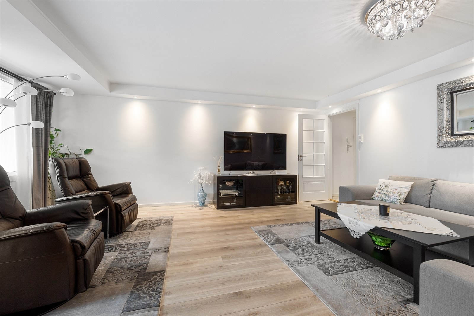 Dagslyset som strømmer inn via store, vestvendte vinduer gjenspeiles fint i de hvitmalte overflatene, og allrommet har tidsmessig laminat på gulvet. Galleribilde