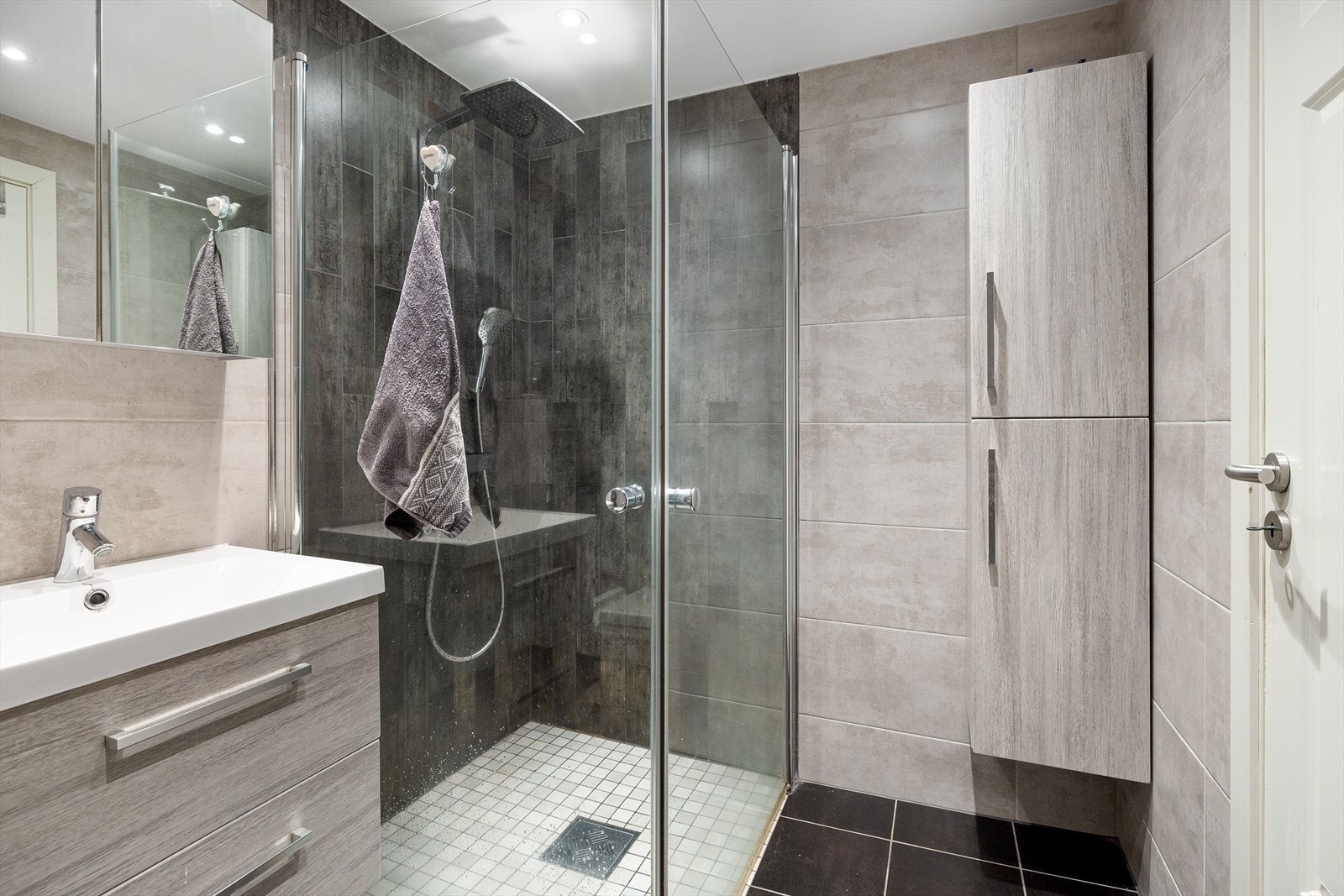 Baderomsinnredningen har lyse, finerte fronter og består av en heldekkende servant på en skuffeseksjon, et høyskap og et dobbelt speilskap. Galleribilde