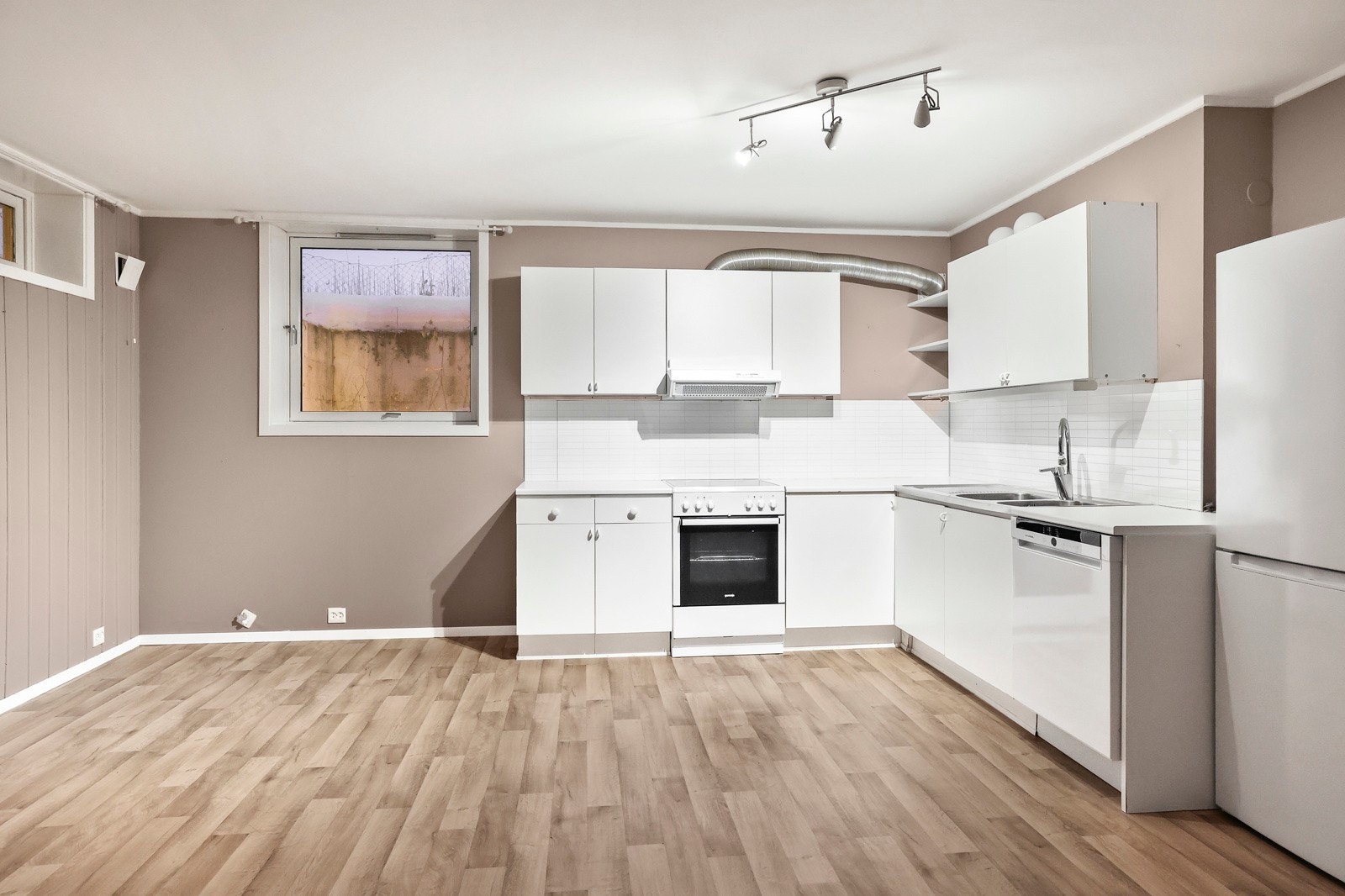 Det er frittstående komfyr, oppvaskmaskin, og kjøleskap med fryser. Mellom kjøkkenbenk og overskap er det en laminert plate. Galleribilde