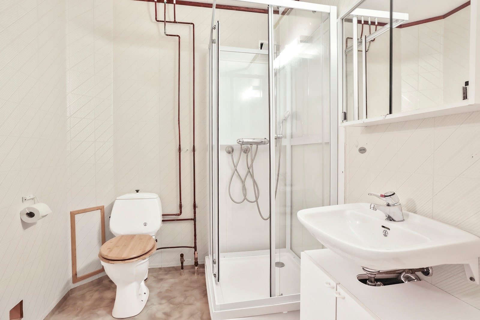 Badet i kjelleren har gulvbelegg på gulv og baderomsplater og tapet på vegger. Det er gulvstående servantinnredning med skuffer, og speilskap med overlys og stikkontakt Galleribilde