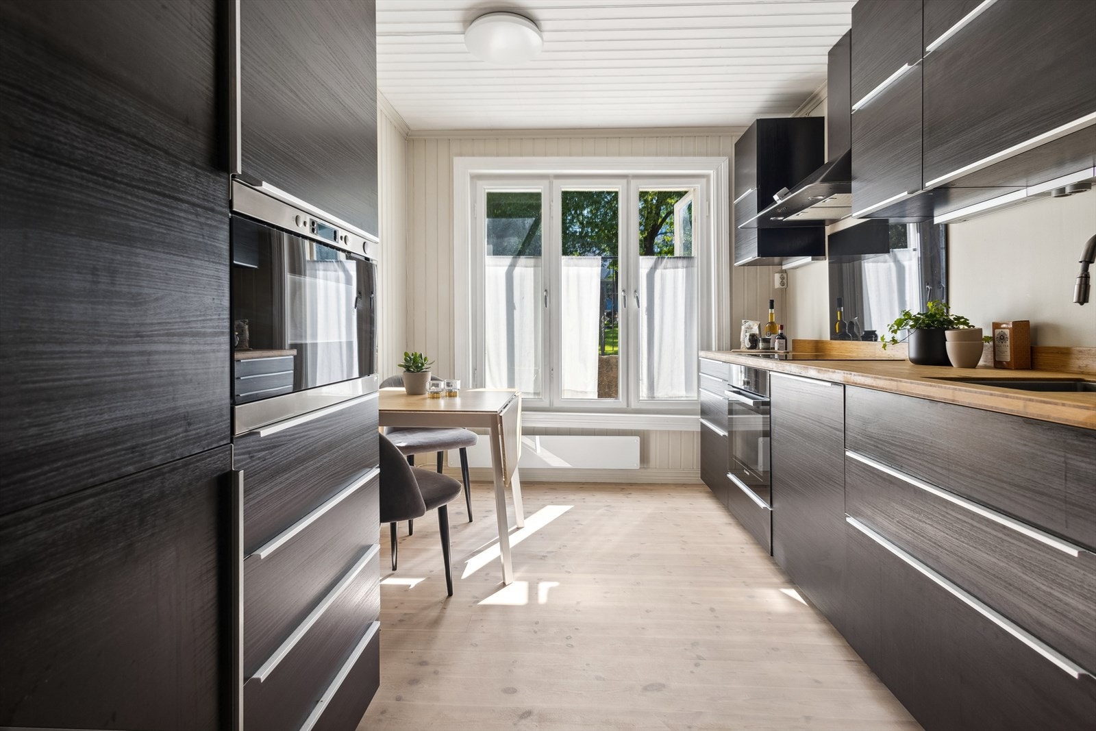 Glassplate på vegg over platetopp. Heltre benkeplate med underlimt kum i rustfritt stål. Kullfilterventilator. Stekeovn, keramisk topp, oppvaskmaskin, mikro og kjøl/frys er integrert i innredningen. Galleribilde