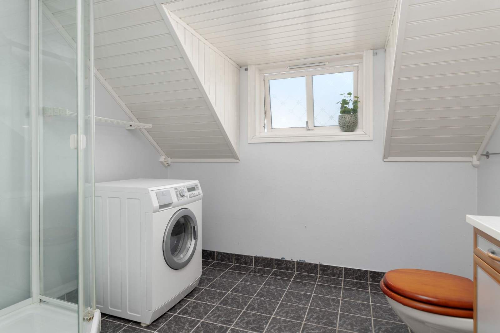 Bad/vaskerom med opplegg for vaskemaskin. Gulvet er flislagt og har elektriske varmekabler. Galleribilde