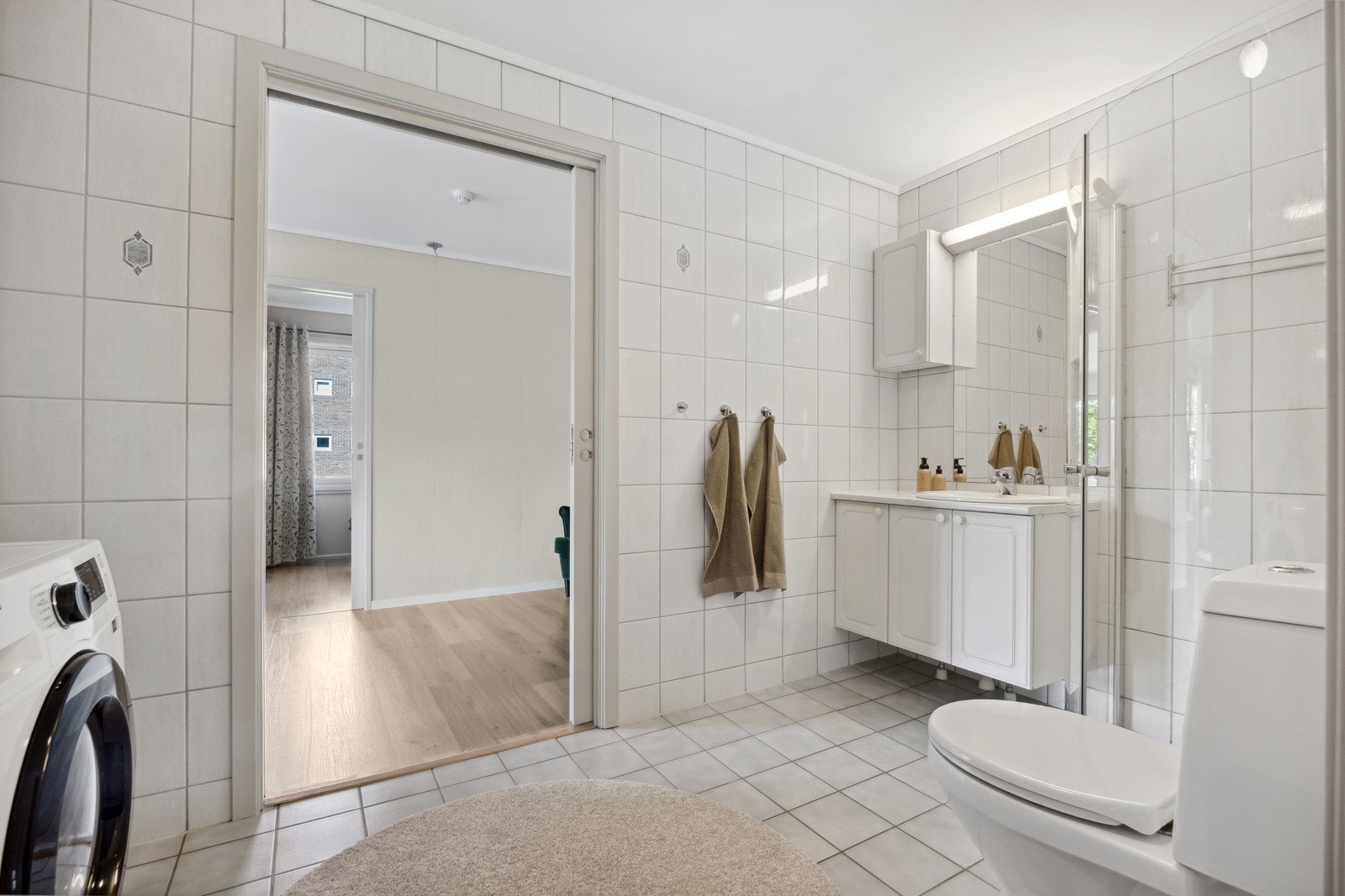 Flislagt baderom utstyrt med vegghengt servantinnredning, dusjhjørne og toalett. Galleribilde