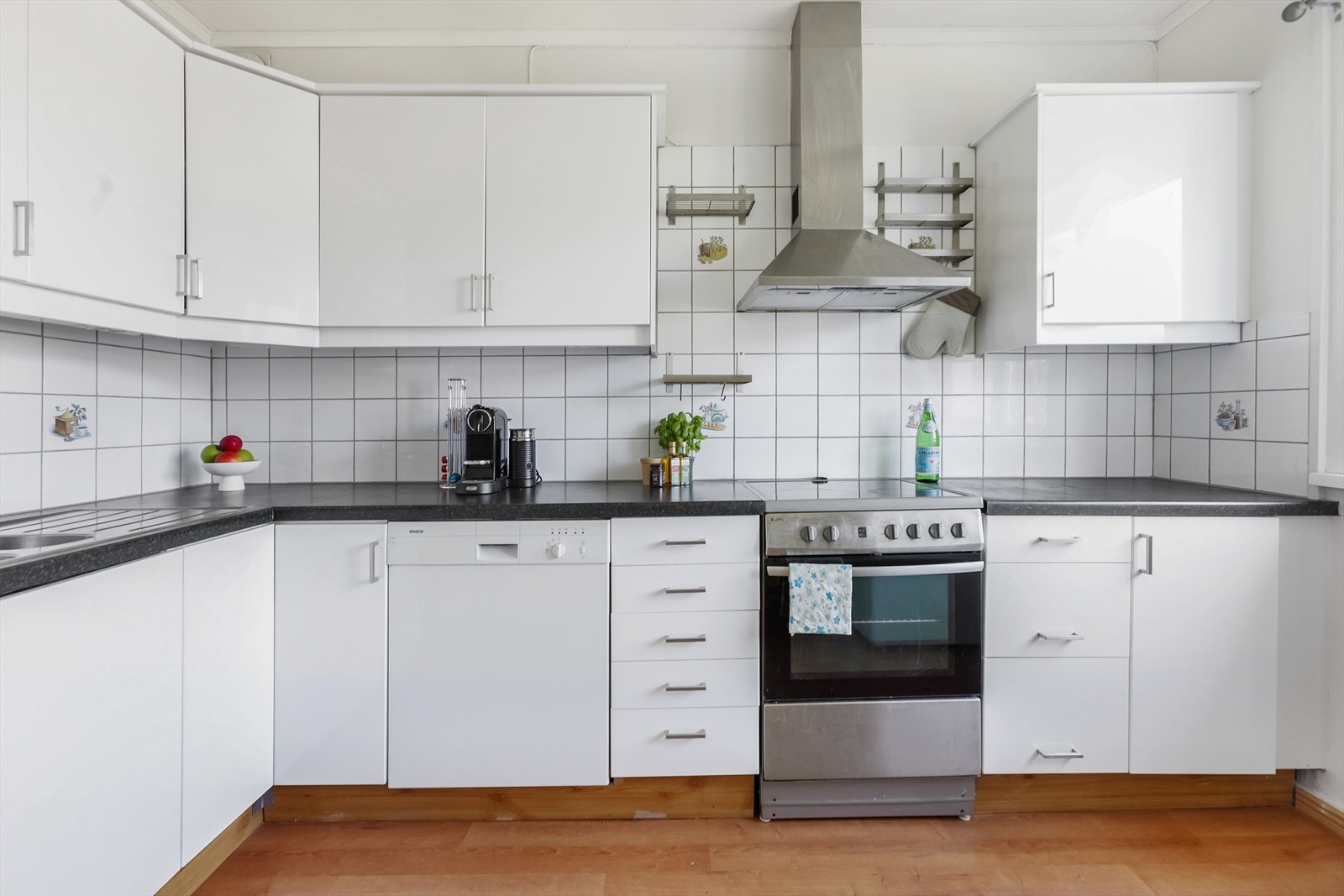 Kjøkkenet er lyst og romslig, og har store vinduer som sørger for rikelig med naturlig dagslys. Kjøkkenet har innredning med glatte, hvite fronter. Benkeplaten er laget av laminat og har en nedfelt oppvaskkum med et ettgreps blandebatteri. Galleribilde