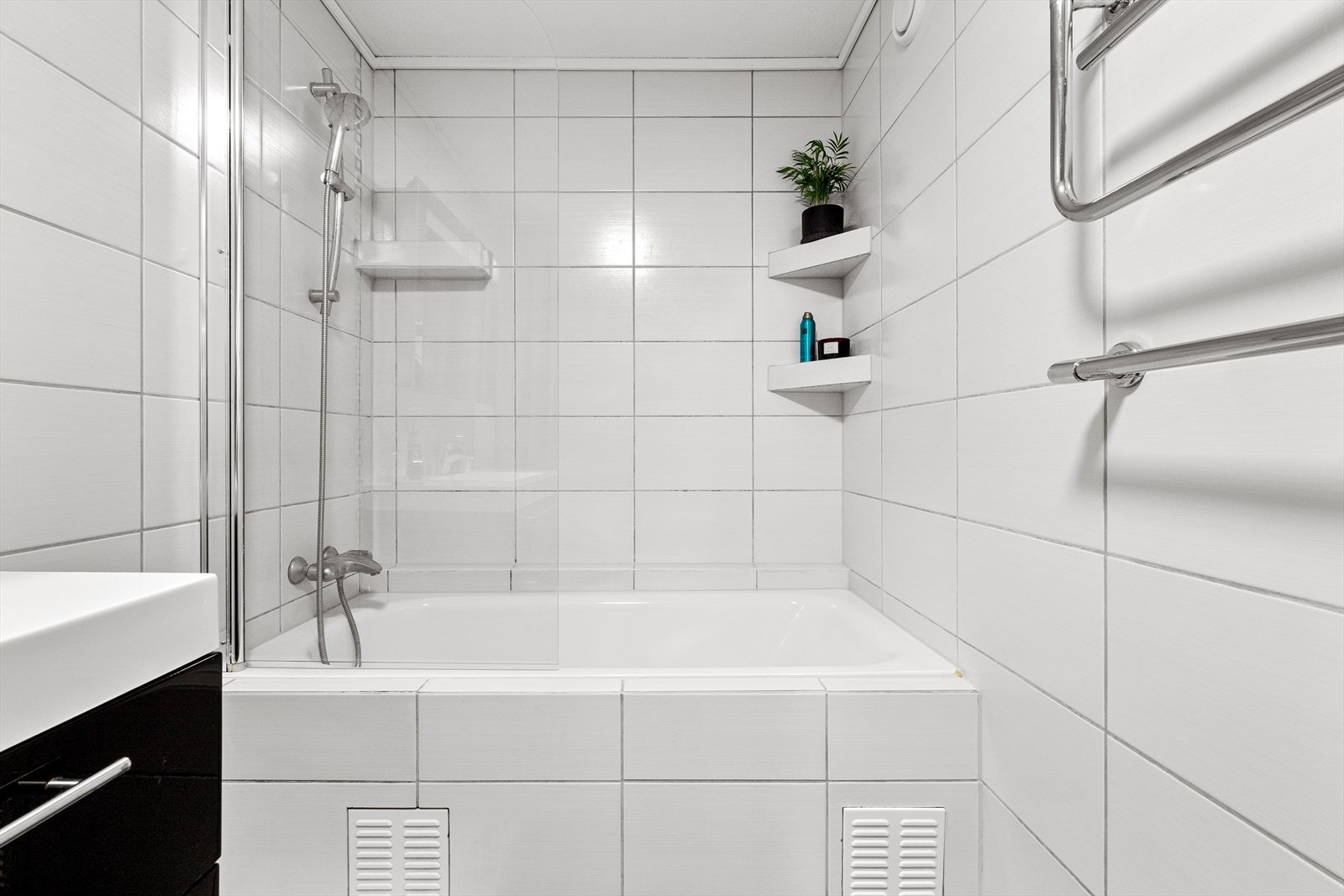 Badet er smakfullt innredet med fliser på både gulv og vegger og moderne innredning med servant med svarte underskuffer, speil med skap og lys, samt et deilig badekar. Galleribilde