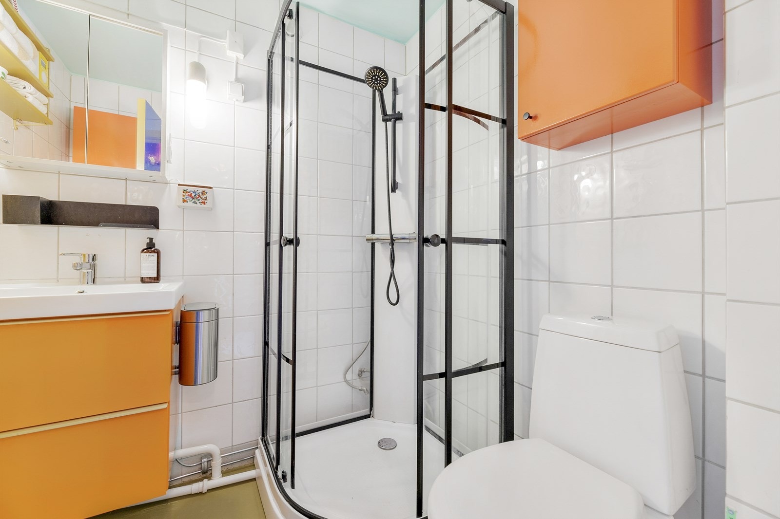 Badet er utstyrt med dusjkabinett, gulvmontert WC, nedsunket servant med skap, speilskap og veggmontert skap som gir ekstra lagringsplass Galleribilde