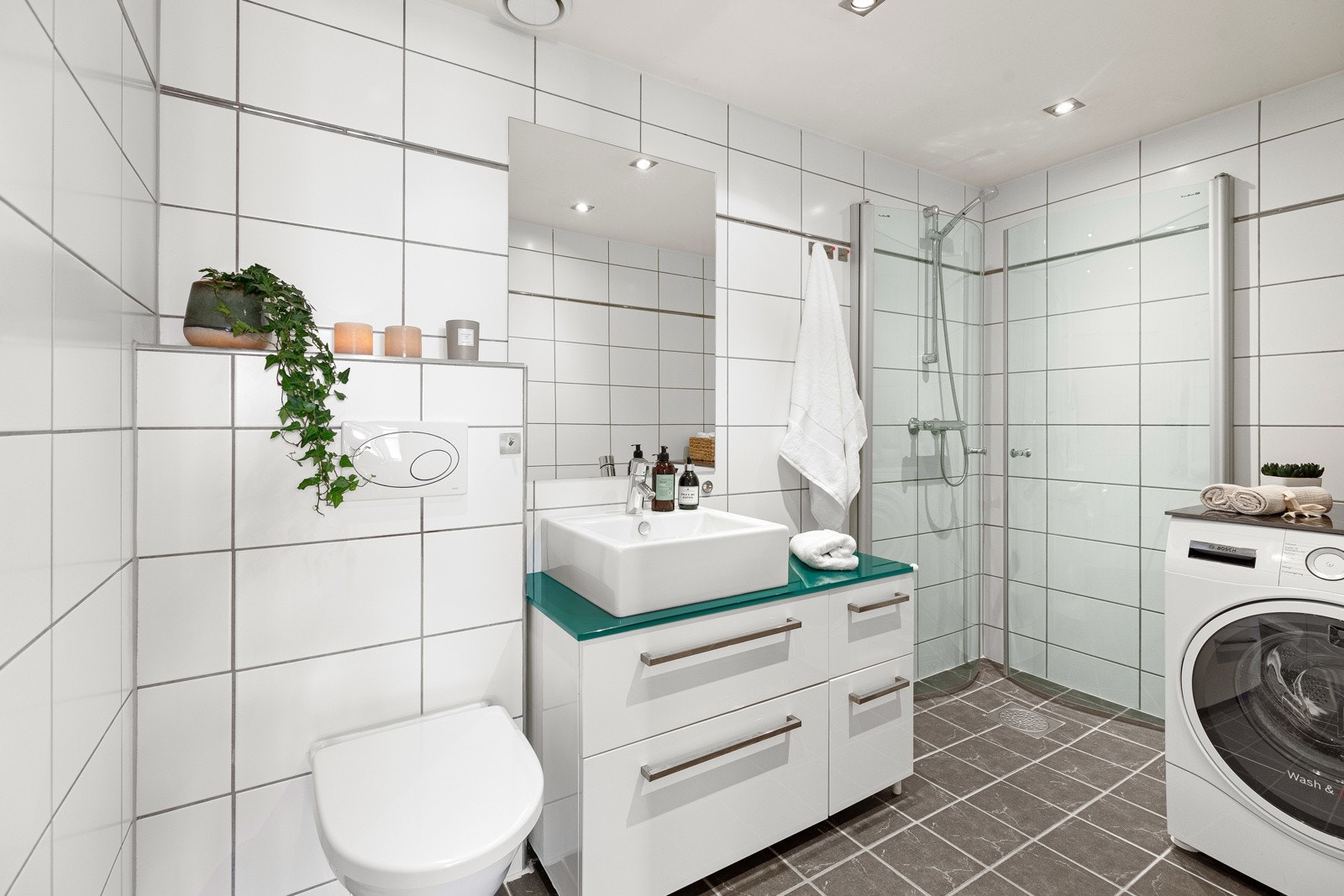 Flislagt bad med dusjhjørne, veggmontert servantinnredning og toalett samt opplegg for vaskemaskin Galleribilde