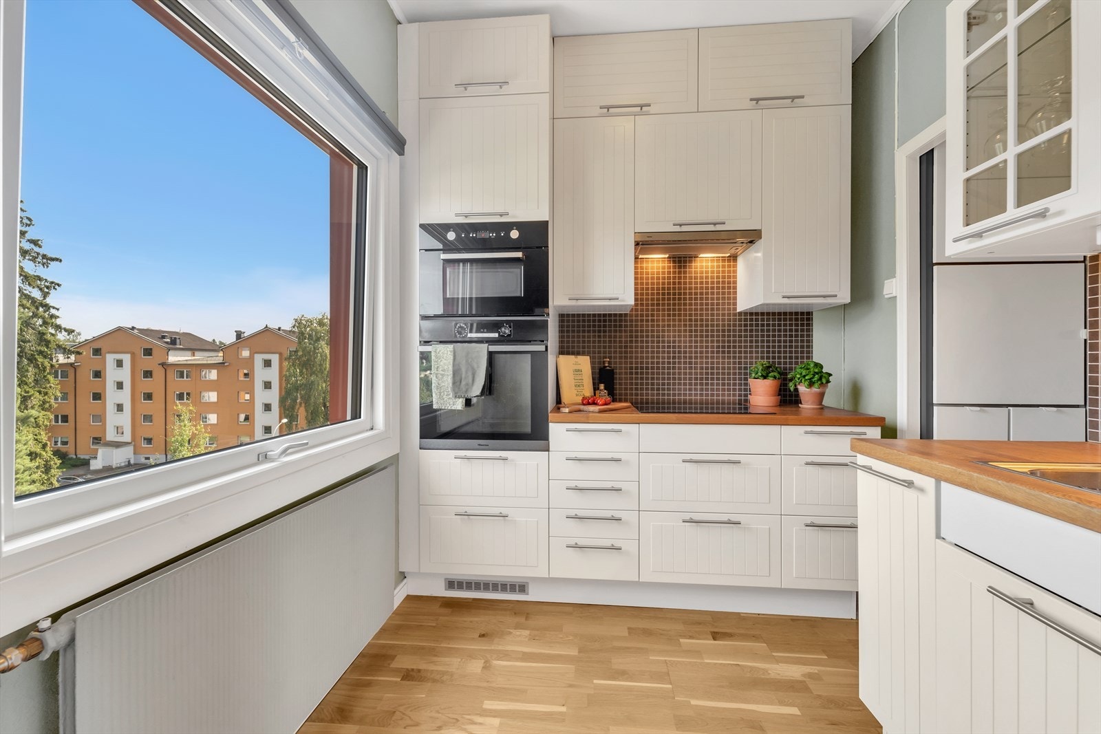 Kjøkkeninnredning med profilerte lakkerte fronter, heltre eik benkeplate med fliser over, oppvaskkum og ventilator samt integrerte hvitevarer som stekeovn, koketopp, mikroovn, oppvaskmaskin, kjøleskap og fryseskap. Galleribilde