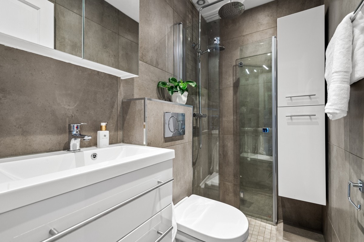 Badet ble pusset opp i 2021 og er utstyrt med dusjhjørne, oppbevaringsskap, vegghengt klosett og heldekkende servant med skuffer Galleribilde