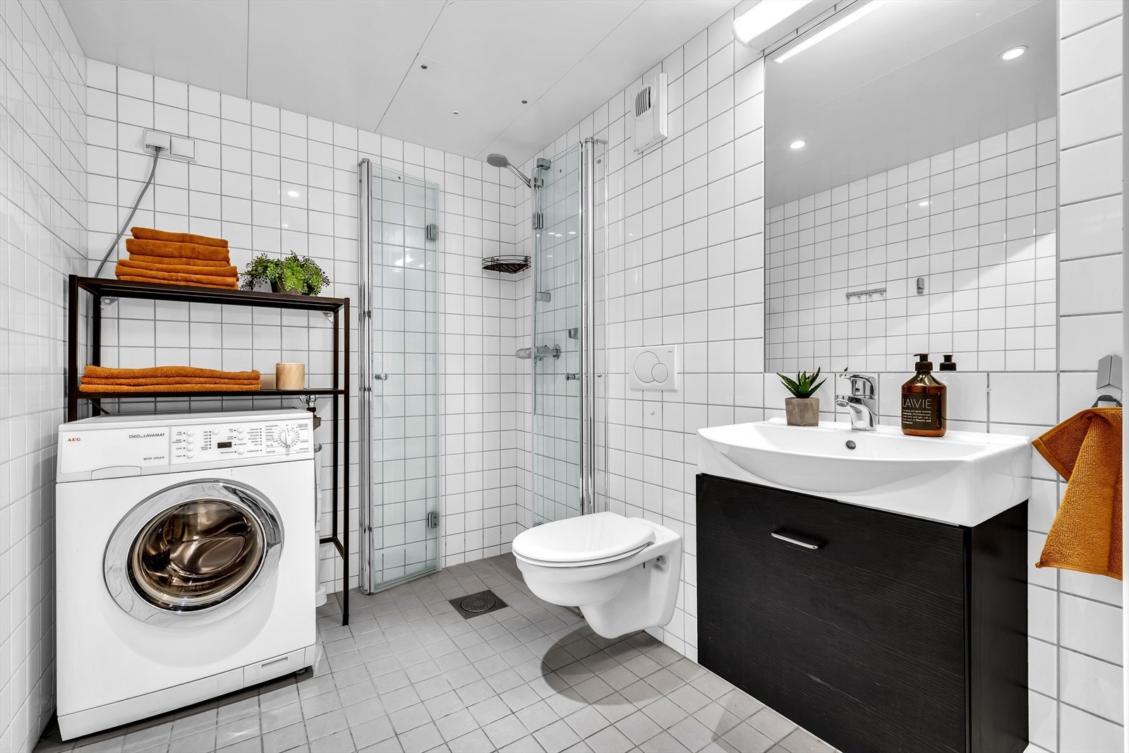 Et romslig bad med dusjhjørne, stående klossett og opplegg for vaskemaskin og tørketrommel Galleribilde
