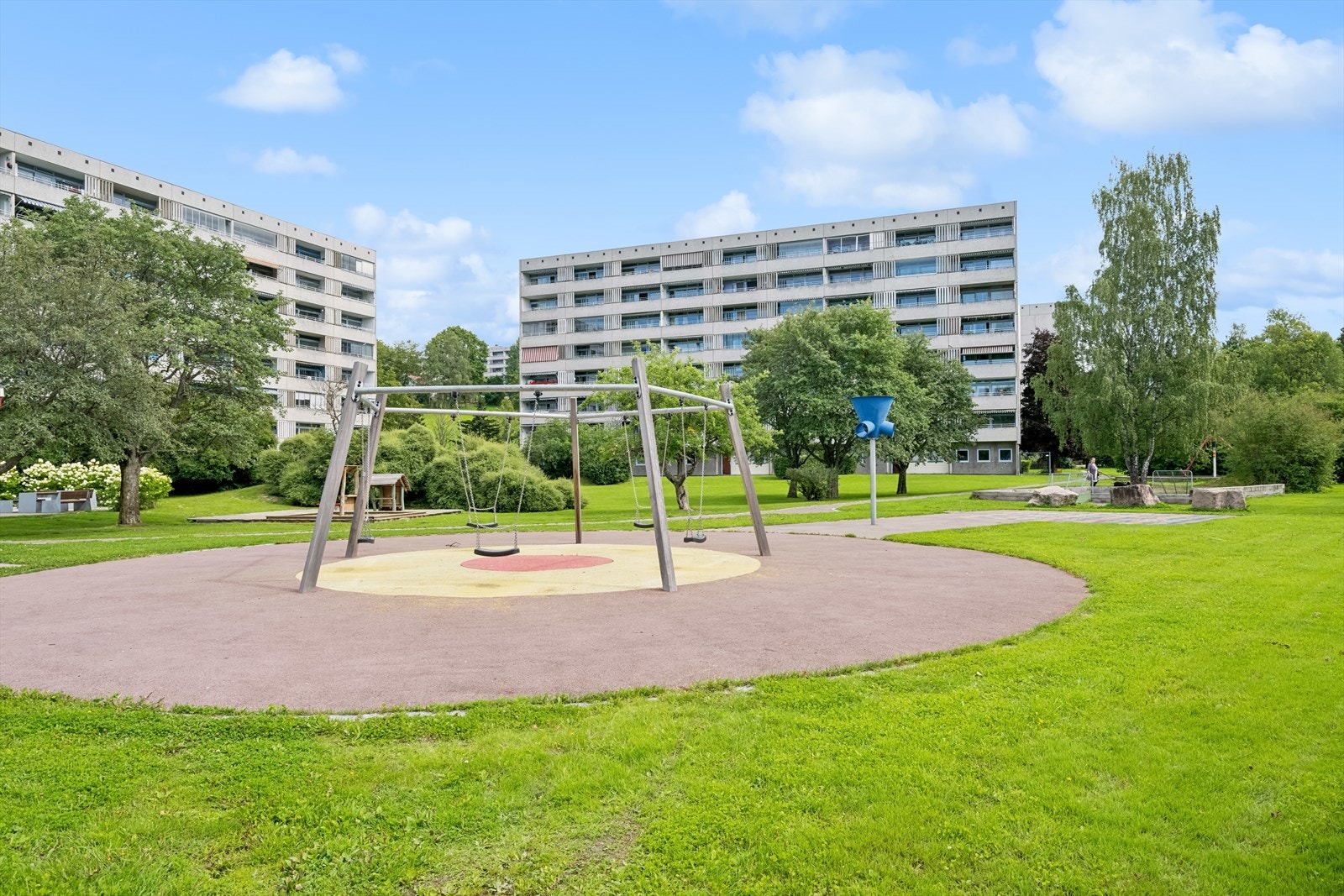 Stort fellesareal opparbeidet med asfalterte adkomstveier/ plasser, gressplen, beplantning, trær, lekeapparater, parkeringsarealer m.m. Galleribilde