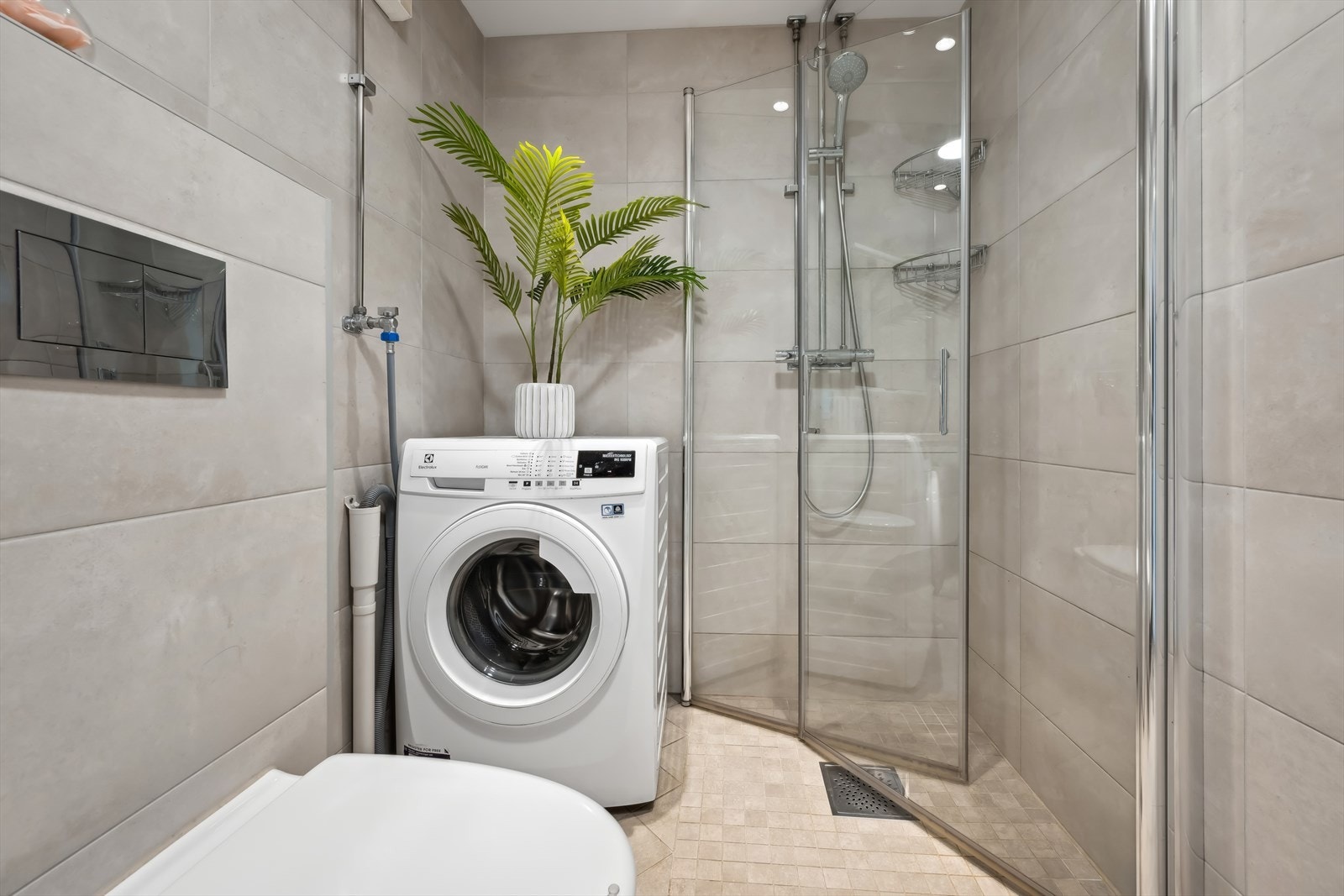 Videre er badet innredet med et elegant dusjhjørne med to svingbare glassdører og et brukervennlig 2-greps blandebatteri. Det vegghengte toalettet gir et rent og moderne uttrykk. I tillegg er det opplegg for vaskemaskin. Galleribilde