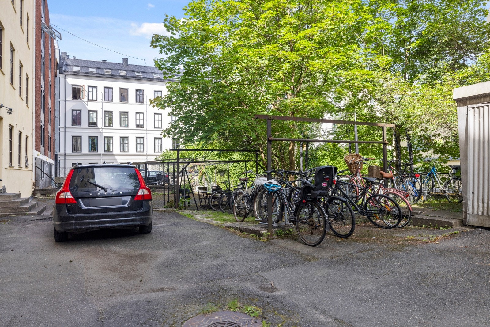 Fellestomten har en inngjerdet forhage med gress og vakre trær. På baksiden er det asfaltert gårdsplass og garasjerekke Galleribilde