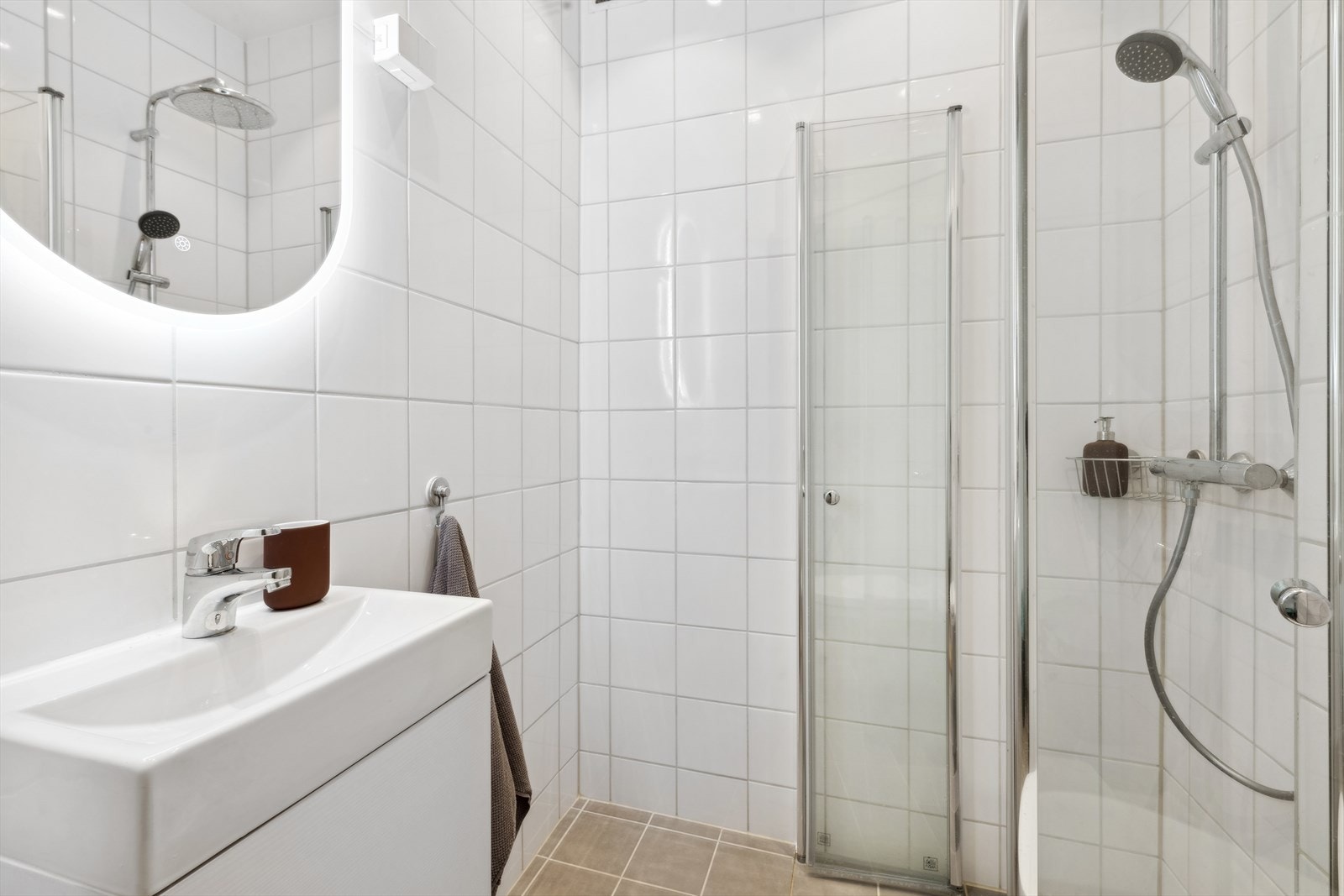 Baderommet er innredet med dusjhjørne, vegghengt toalett, servant med underskap og speil med belysning. Galleribilde