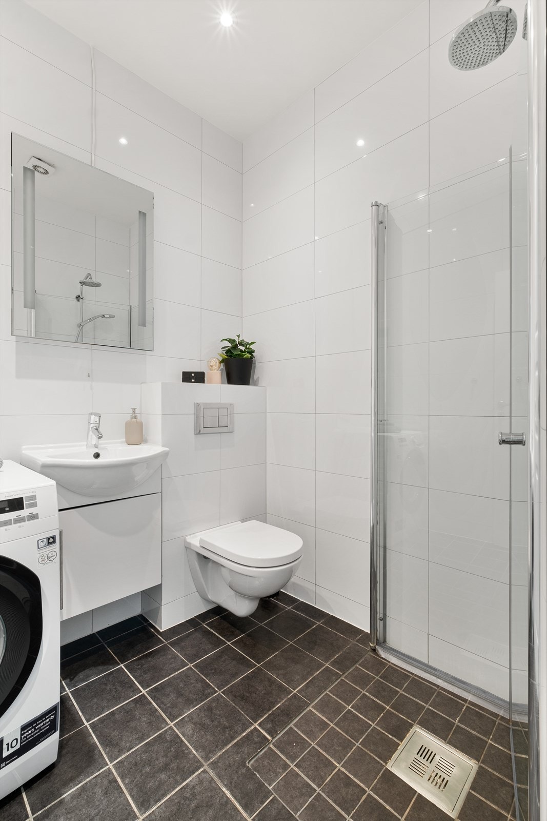 Innredet med vegghengt klosett, servant med innredning, speilskap med lys og dusjhjørne med svingbare glassdører. Opplegg for vaskemaskin. Elektrisk styrt vifte. Galleribilde