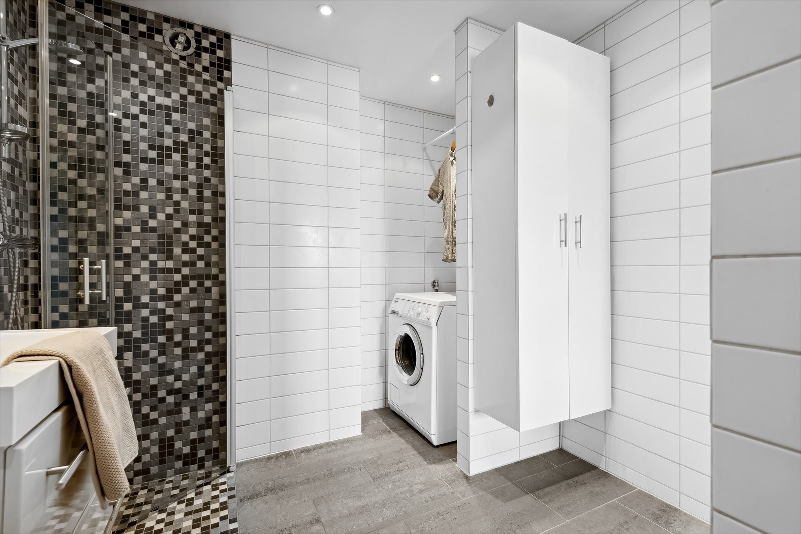 Badet er utstyrt med en innredning med heldekkende servant, speil, veggmontert toalett, dusj med innfellbare dusjdører og opplegg for vaskemaskin. Galleribilde