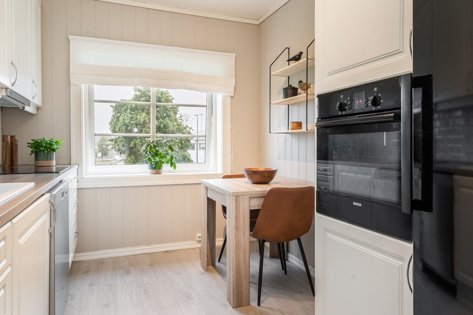 Pent kjøkken med fin spiseplass ved vindu og lys, takhøy kjøkkeninnredning type Ikea. Integrert induksjonstopp og stekeovn i praktisk arbeidshøyde. Galleribilde