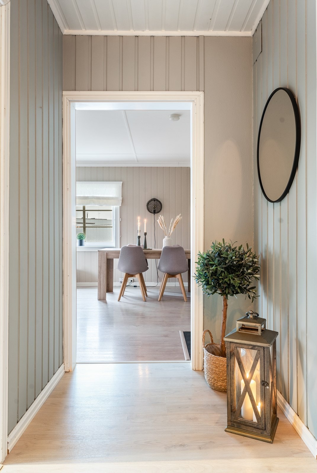 Fin og romslig entré med pen laminat på gulv og panel på vegger, malt opp i en fin, tidsriktig fargetone. Hvitmalt panel i tak. Galleribilde
