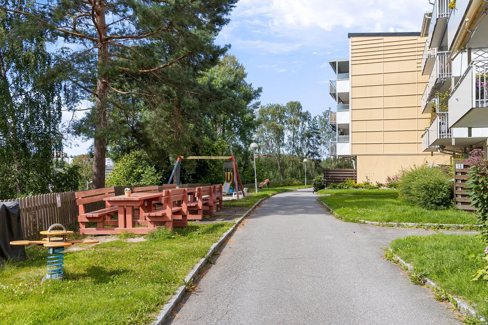 Pent opparbeidet fellesareal med asfalterte internveier og gressplen, samt lekeapparater, sittegrupper og diverse beplantning. Galleribilde