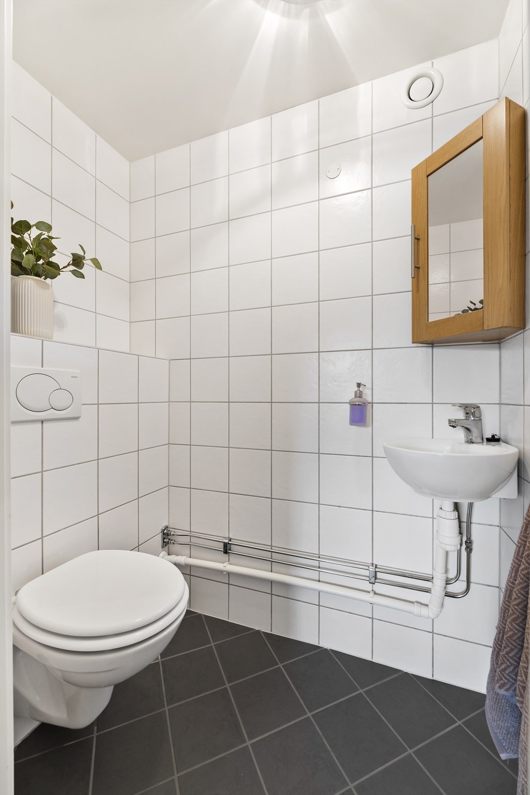 Separat toalettrom fra 2012 med malte plater i tak og flis på gulv og vegg. Rommet er innredet med veggmontert toalett, servant og speil. Galleribilde