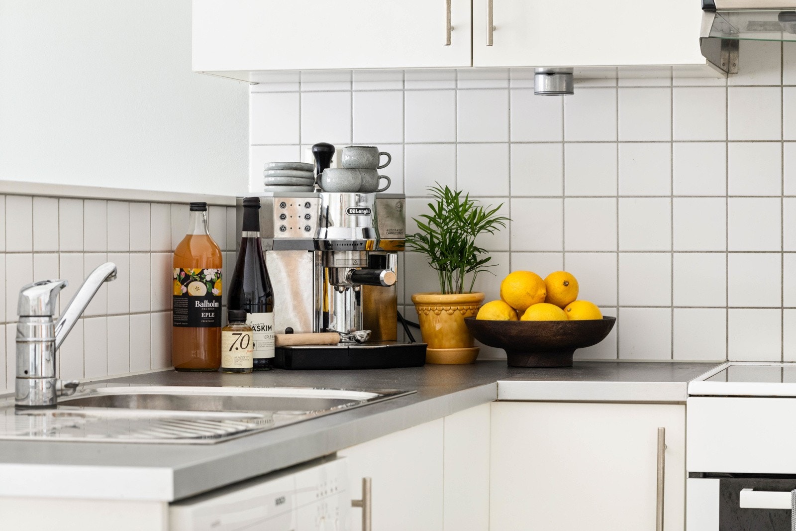 Kjøkkeninnredning med glatte fronter og laminat benkeplater. Nedfelt rustfri oppvaskkum og fliser mellom benk og overskap. Galleribilde