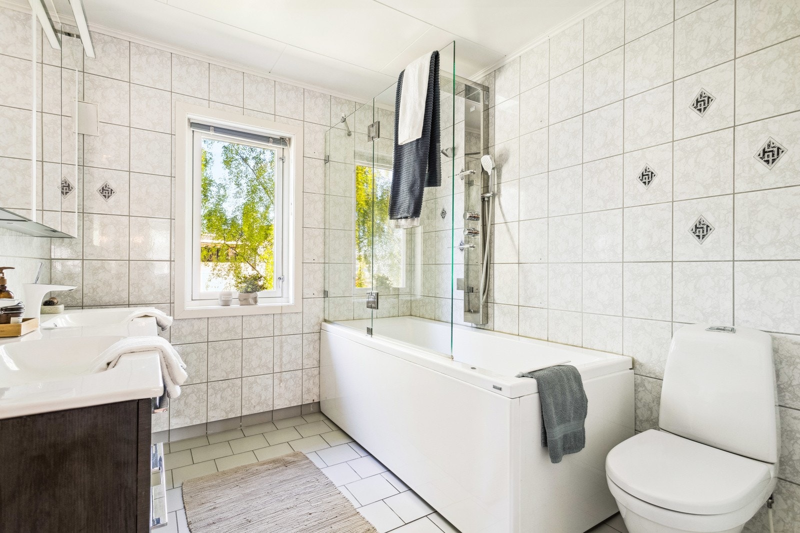 Badet har badekar med vegghengt dusjarmatur. Baderomsinredning og toalett. Galleribilde