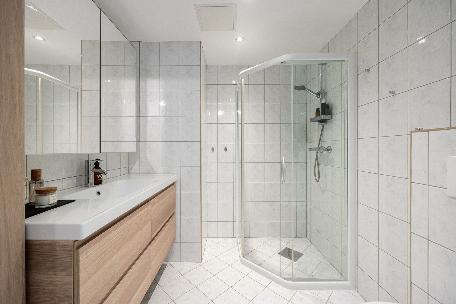 Badet er holdt i en tidløs stil med hvite veggfliser og gulvfliser. Videre er det downlights, gulvvarme og vegghengt toalett. Galleribilde