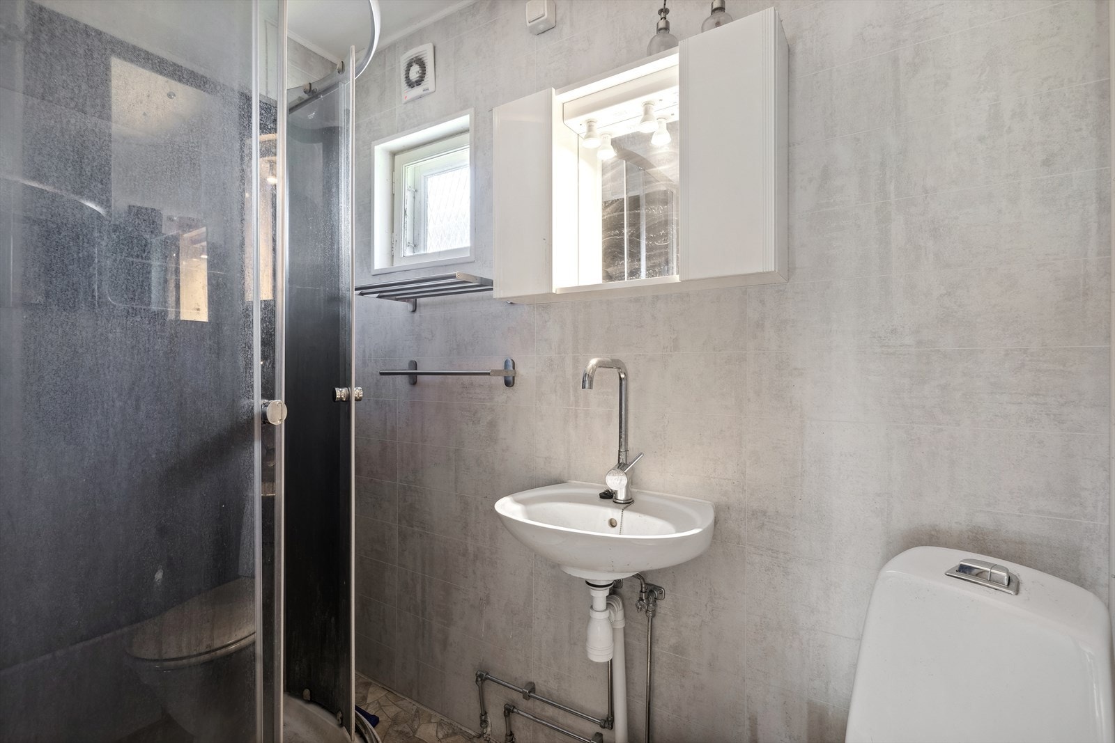 Hytta har et baderom med vinylbelegg på gulv og vegger kledd med våtromsplater. Badet er innredet med et toalett, enkel servant, overskap med speil og dusjkabinett. Galleribilde