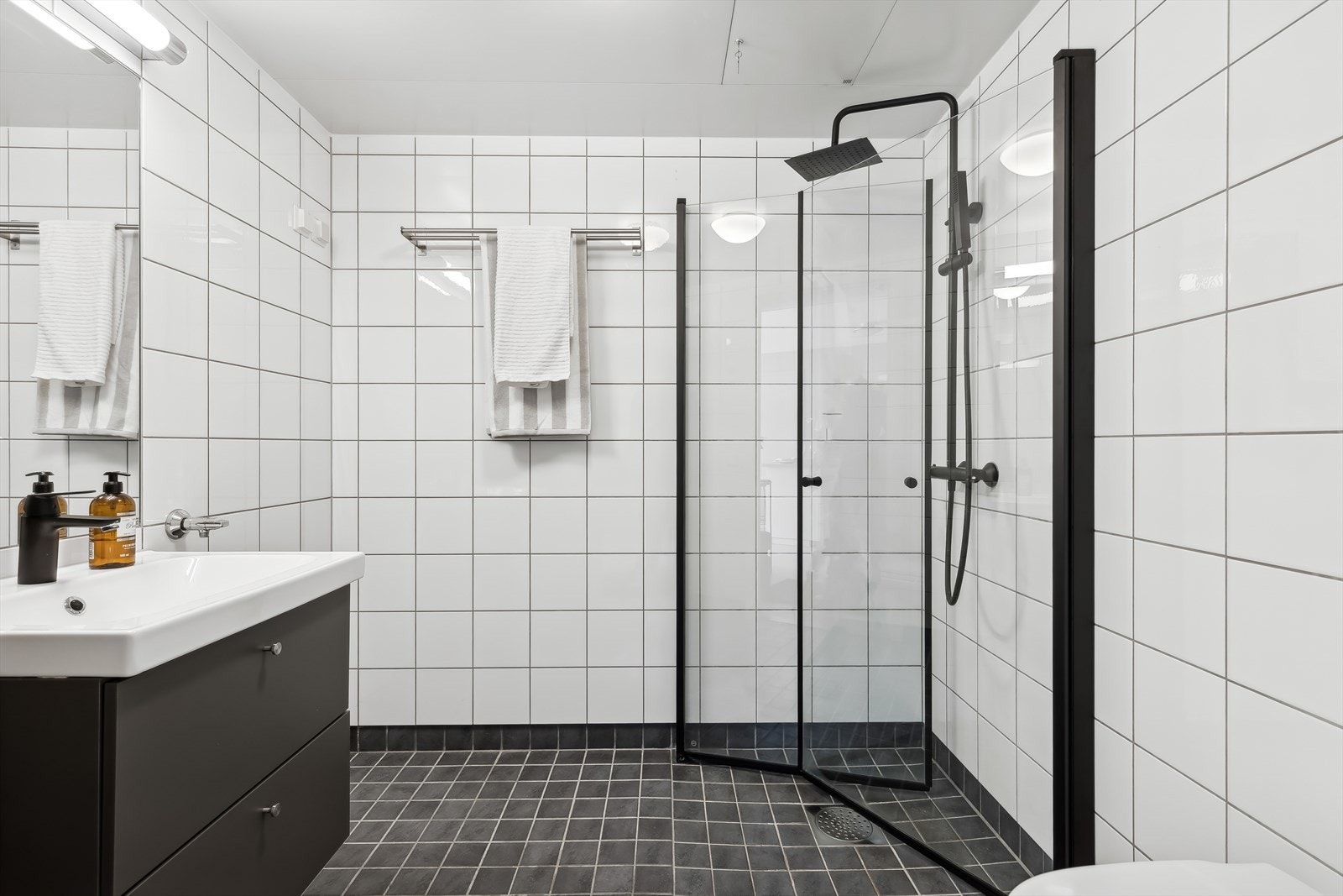 Lekkert bad med flislagte vegger og gulv med varmekabler. Badet består av dusj med innfellbare dører i herdet glass, servant, veggfestet klosett med innebygget sisterne og opplegg for vaskemaskin. Galleribilde