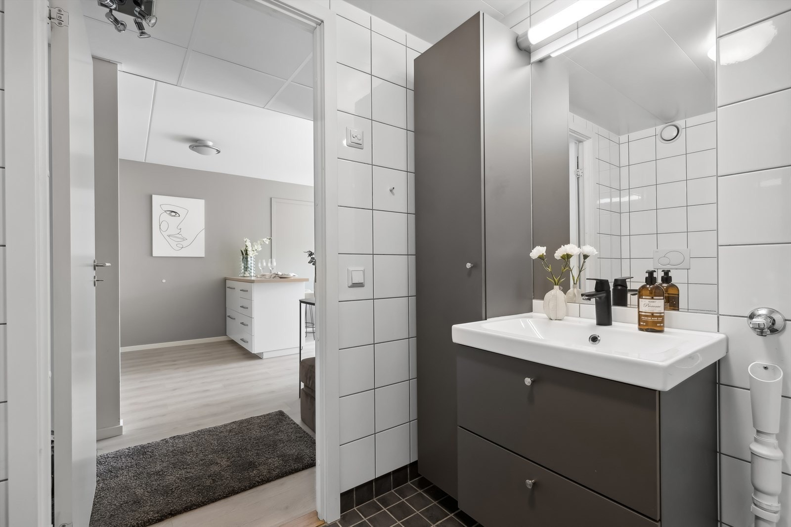 Baderomsinnredning bestående av benkeskap og høyskap med glatte fronter. Speil og belysning over servant. Galleribilde