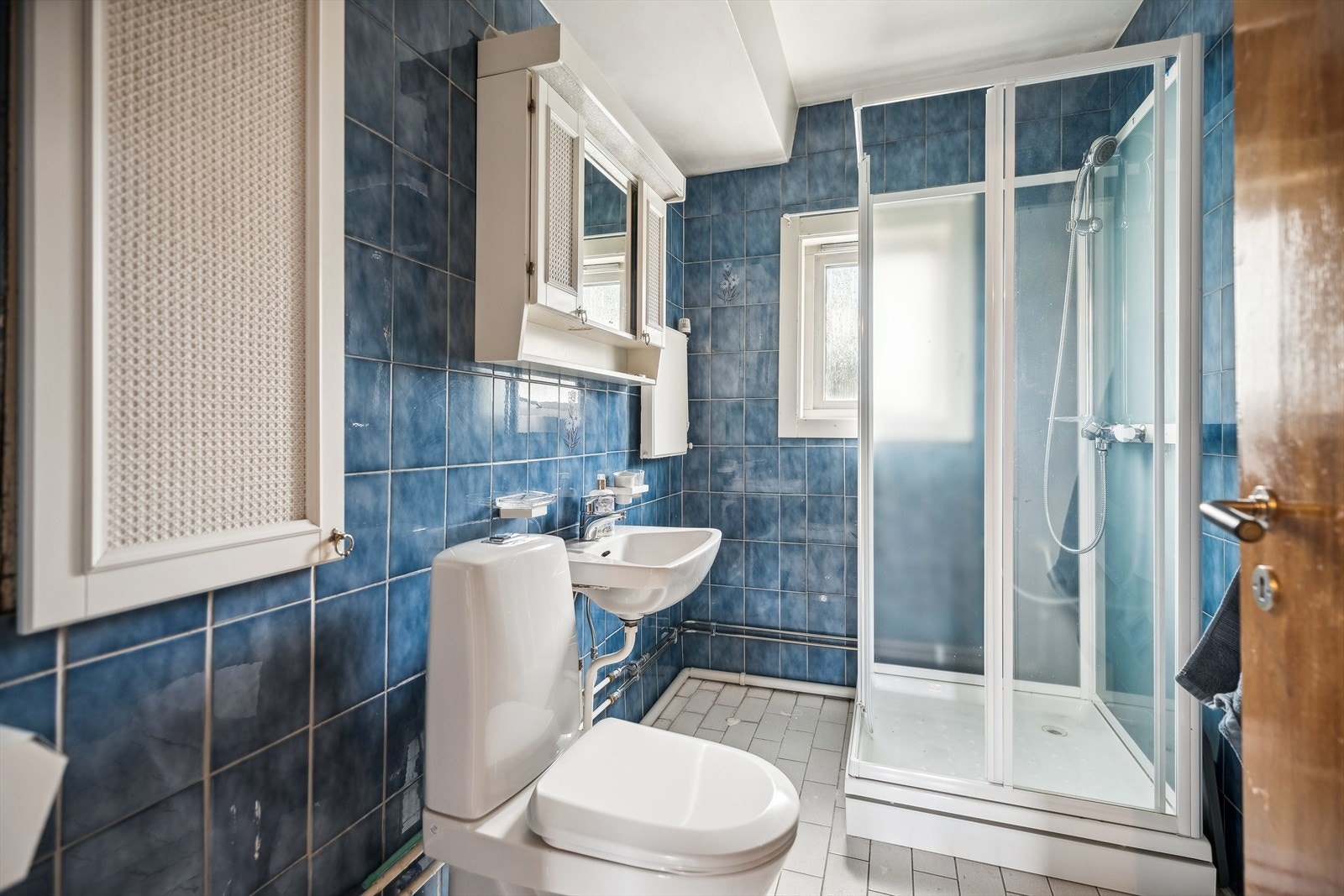 Badet er av eldre dato, utstyrt med dusj, toalett og servant med underskap. Galleribilde