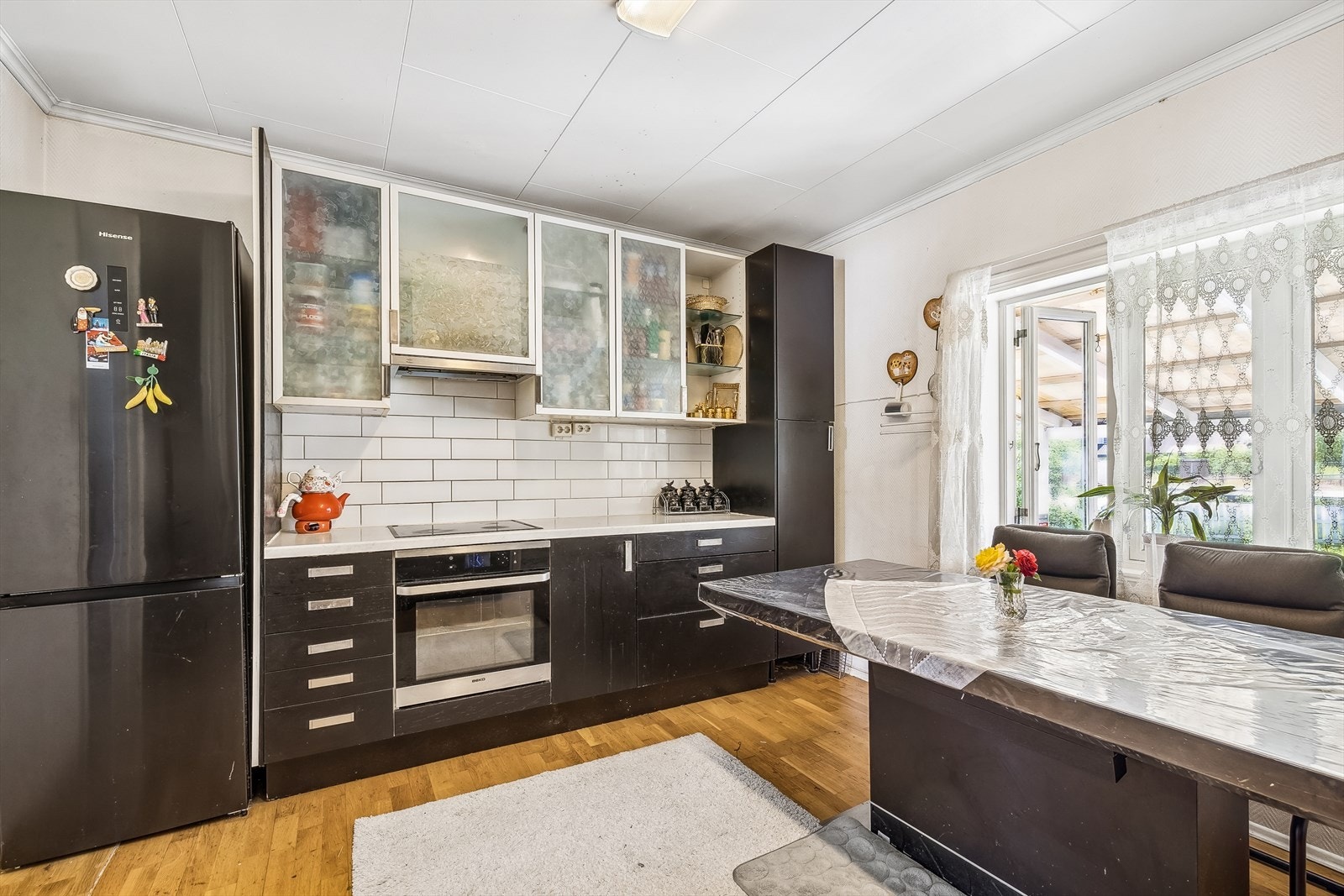 Kjøkkenet inneholder innredning med svarte glatte fronter. Noen fronter av glass. Hvit laminert benkeplate. Integrert koketopp og komfyr. Galleribilde