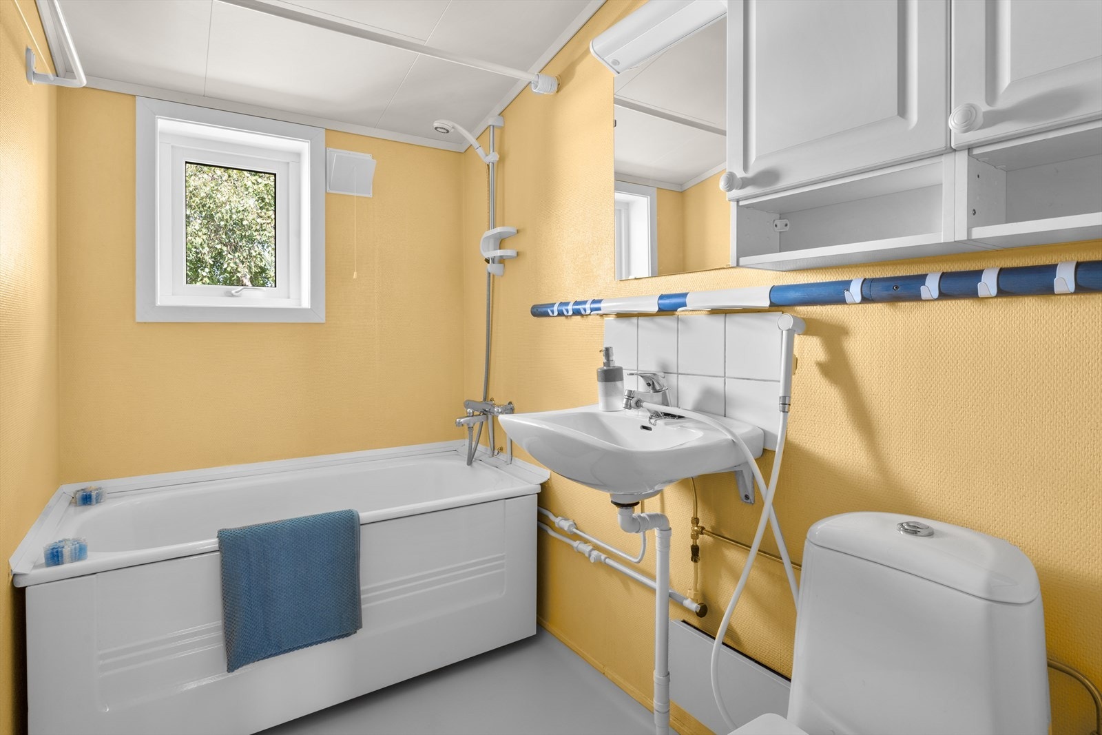 - Romslig baderom med strietapet på veggene og malt betong på gulvet. Badet er innredet med klosett, servant, speil og badekar med forheng. Det ble satt inn nytt toalett i 2024 - Galleribilde