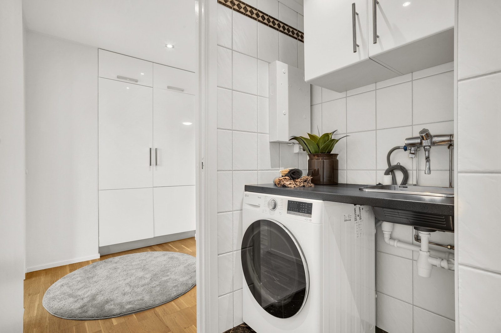 Kran og avløp til vaskemaskin, samt vaskekar med adskilt benkeplate og skap som skaper en egen naturlig vaske-sone. Galleribilde