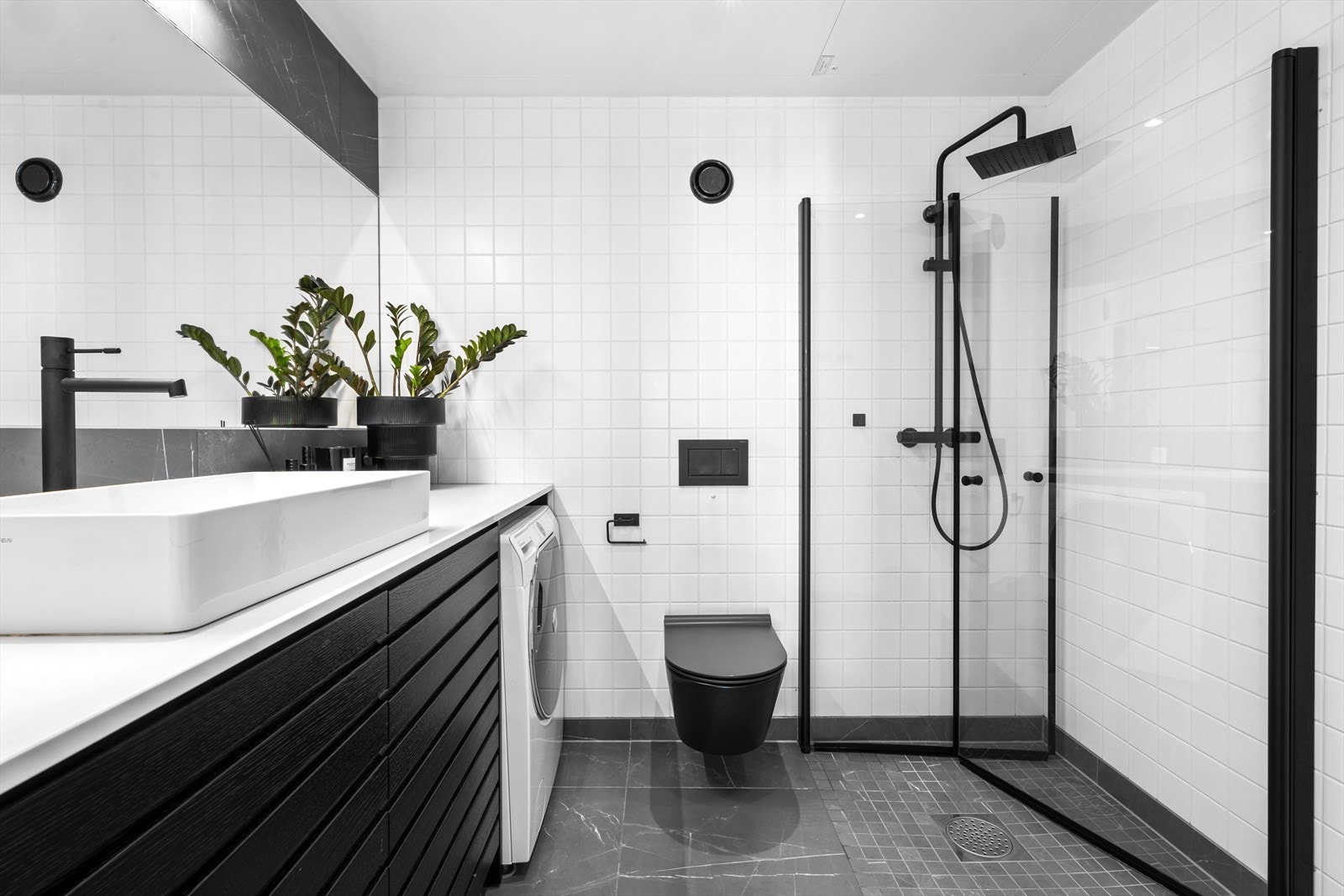 Badet inneholder baderomsinnredning med skuffer og god benkeplass, opplegg for vaskemaskin, vegghengt wc og dusjhjørne med regndusj, hånddusj og glassdører. Galleribilde