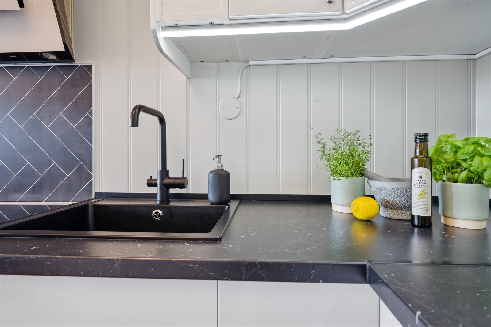 Stilig kjøkken med svart benkeplate og lys under overskap Galleribilde