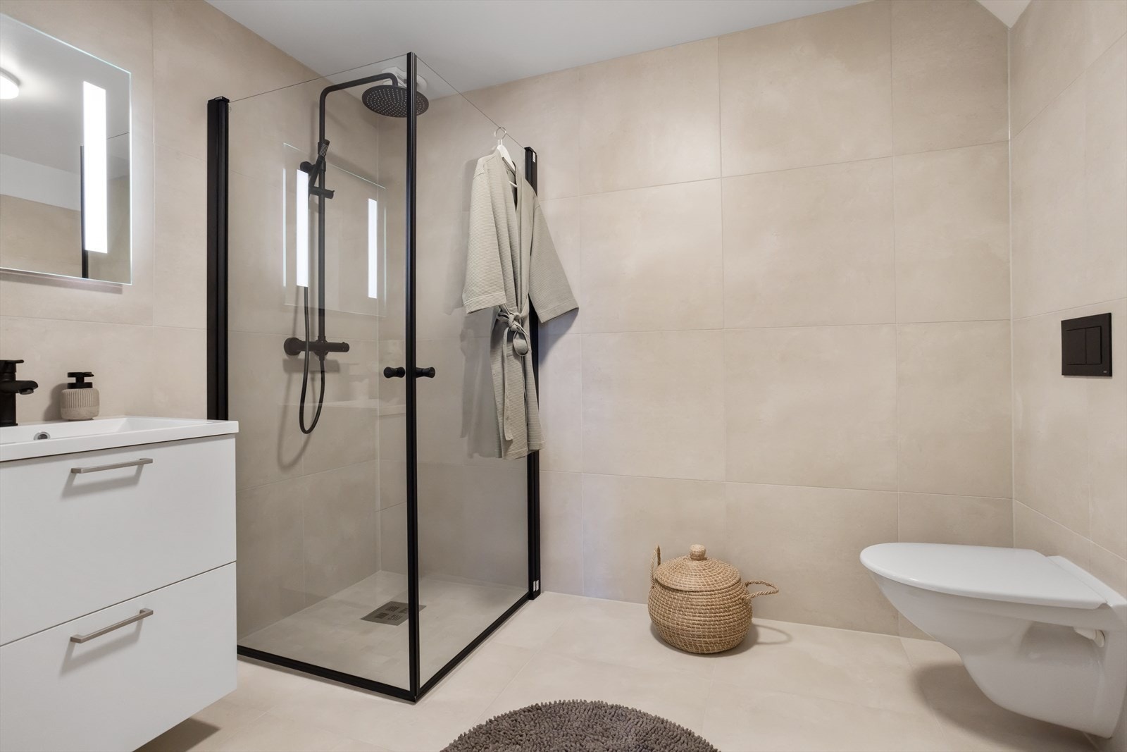 Badet består av dusjhjørne, vegghengt toalett, servant med underskap, og speil med innebygd lys. Galleribilde