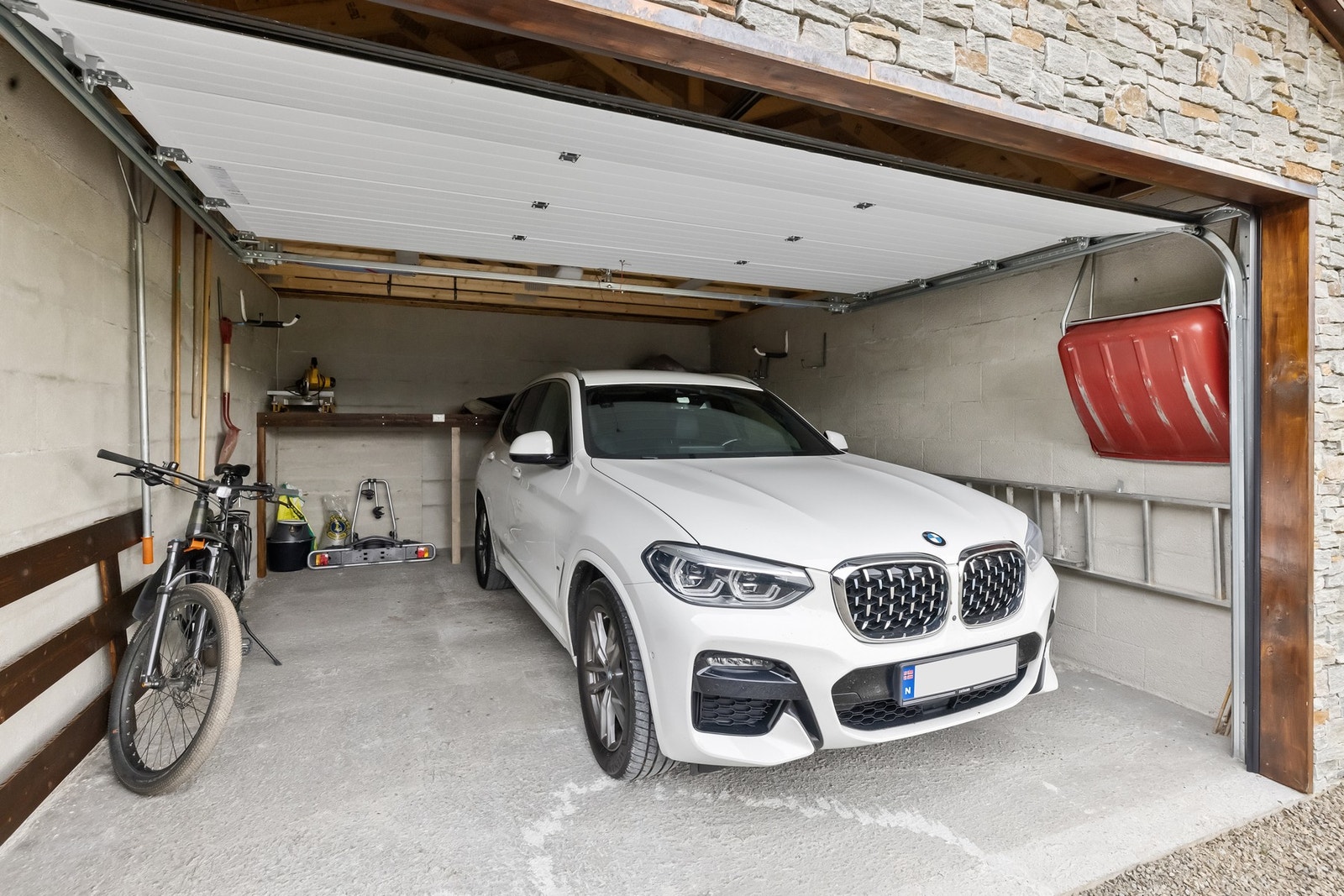 Den frittstående garasjen har god plass til SUV i tillegg til sykler eller andre gjenstander. God takhøyde, innlagt strøm og elektrisk port. Galleribilde