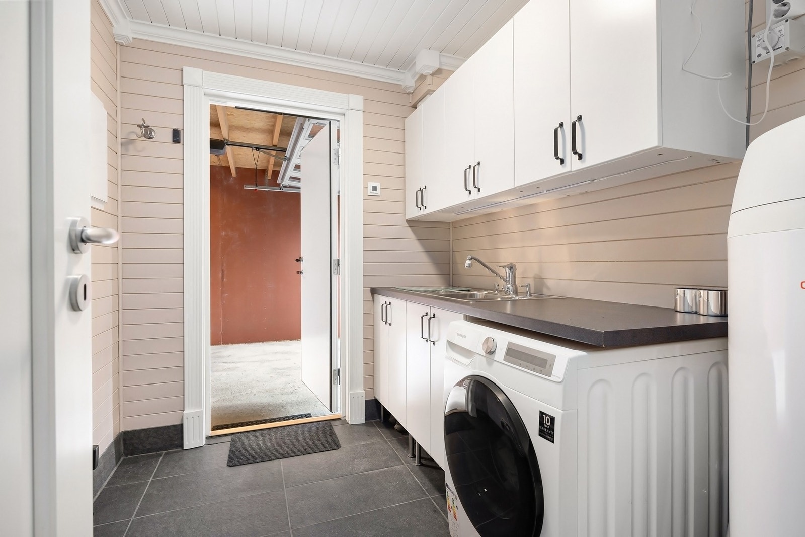 Vaskerom med god skap og benkeplass, plass til vaskemaskin og direkte utgang til garasje. Galleribilde