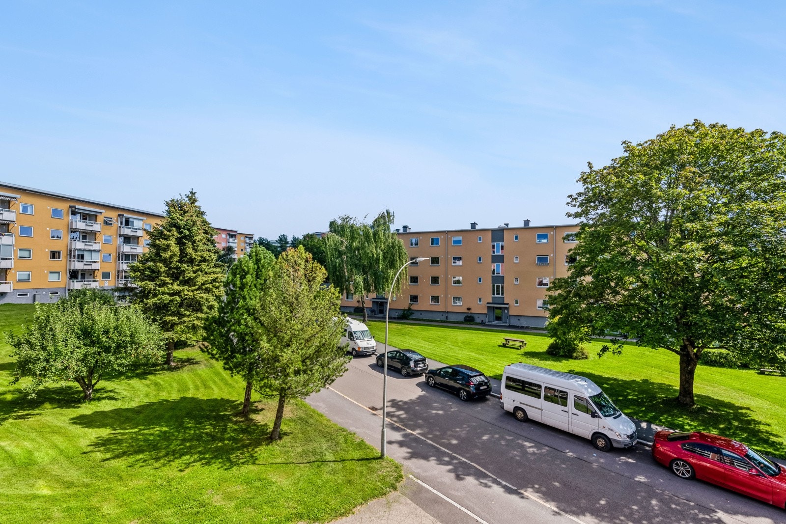 Utsikt fra balkong til flott bearbeidet gressplen og annen baplantning. Galleribilde