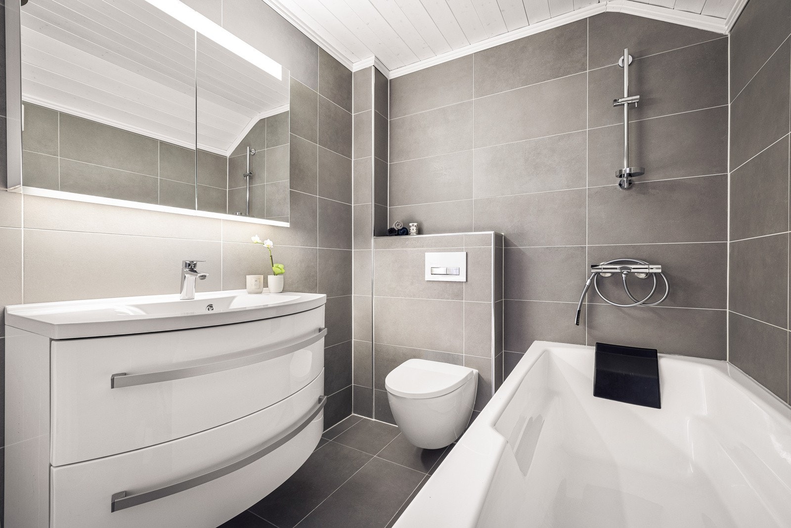 Badet er innredet med veggtoalett, badekar med dusj og baderomsinnredning med heldekkende servant, samt overskap med speilfront og belysning. Galleribilde