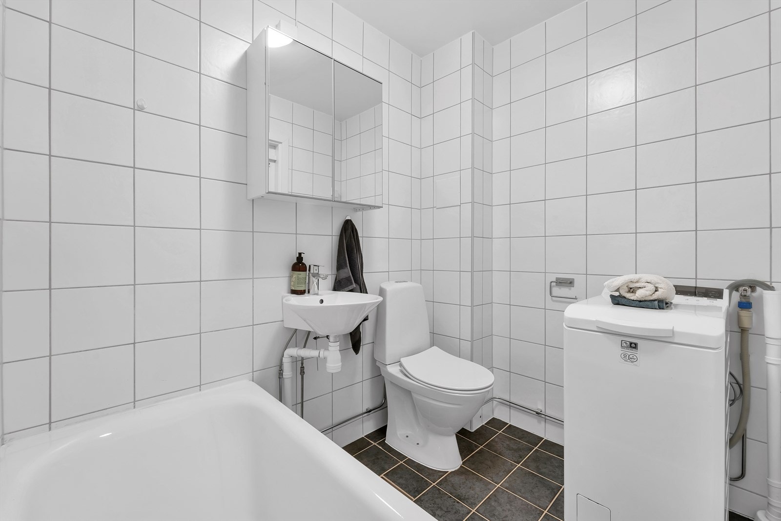 Flislagt bad med varmekabler. Baderomsinnredningen er bestående av vegghengt skaphylle med speil, vegghengt servant og badekar med veggmontert dusjstativ. Gulvmontert WC og opplegg for vaskemaskin. Galleribilde